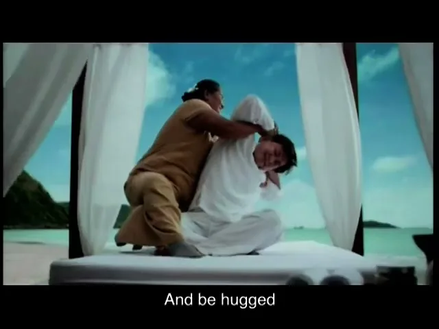 A woman in a brown uniform gives a man in white a massage on a canopy bed on a beach with an ocean view.