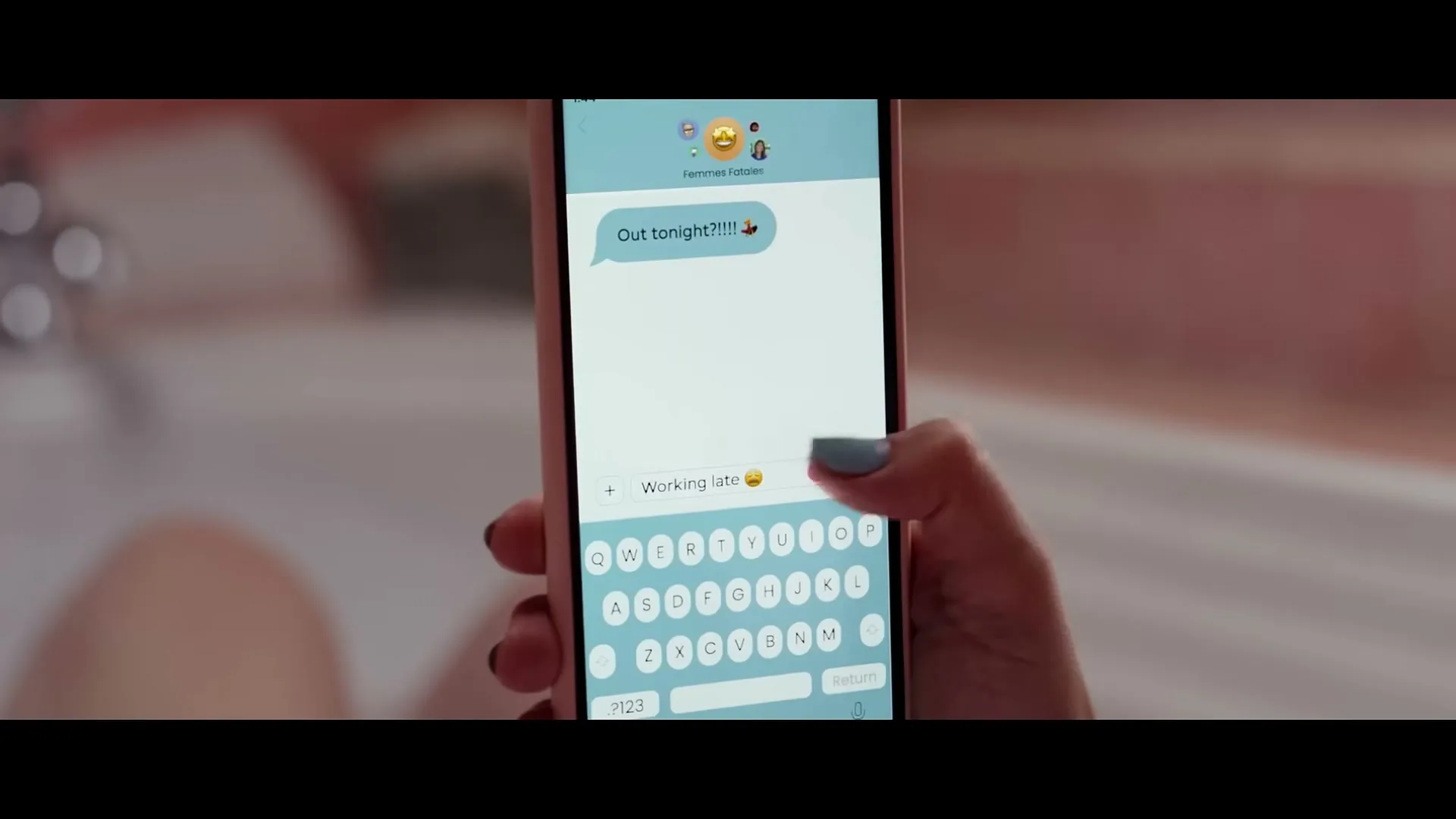 A woman's hand with blue nail polish texts "Working late" on a pink smartphone while in a bathtub.