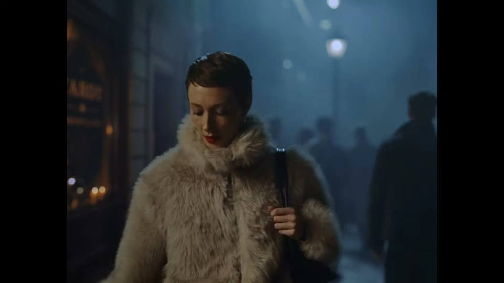 A woman in a white fur coat walks down a foggy street at night, with other people in the background.