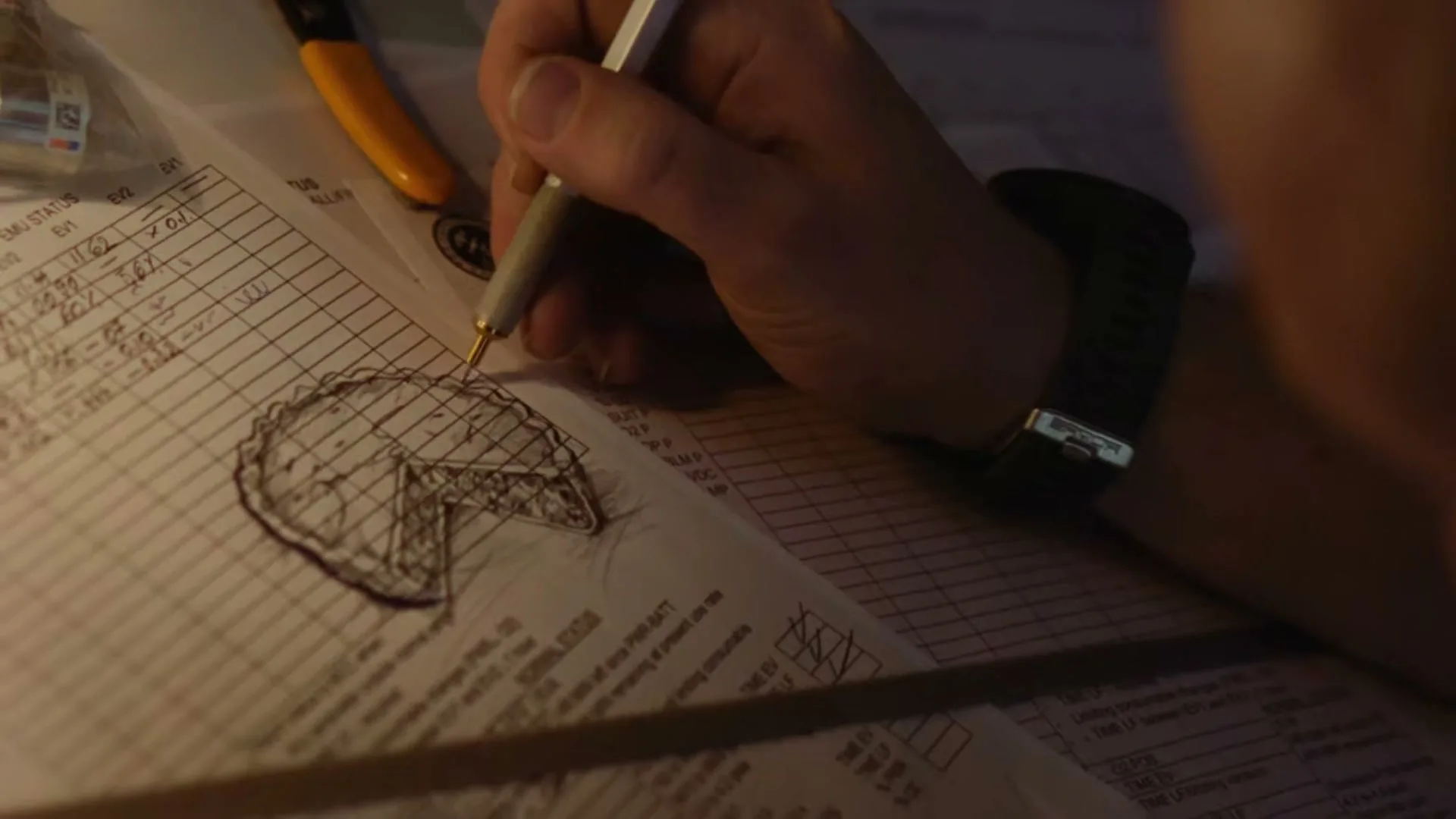 A person's hand draws a detailed sketch of a pie with a slice removed on a piece of paper with technical notes, in a dimly lit interior.