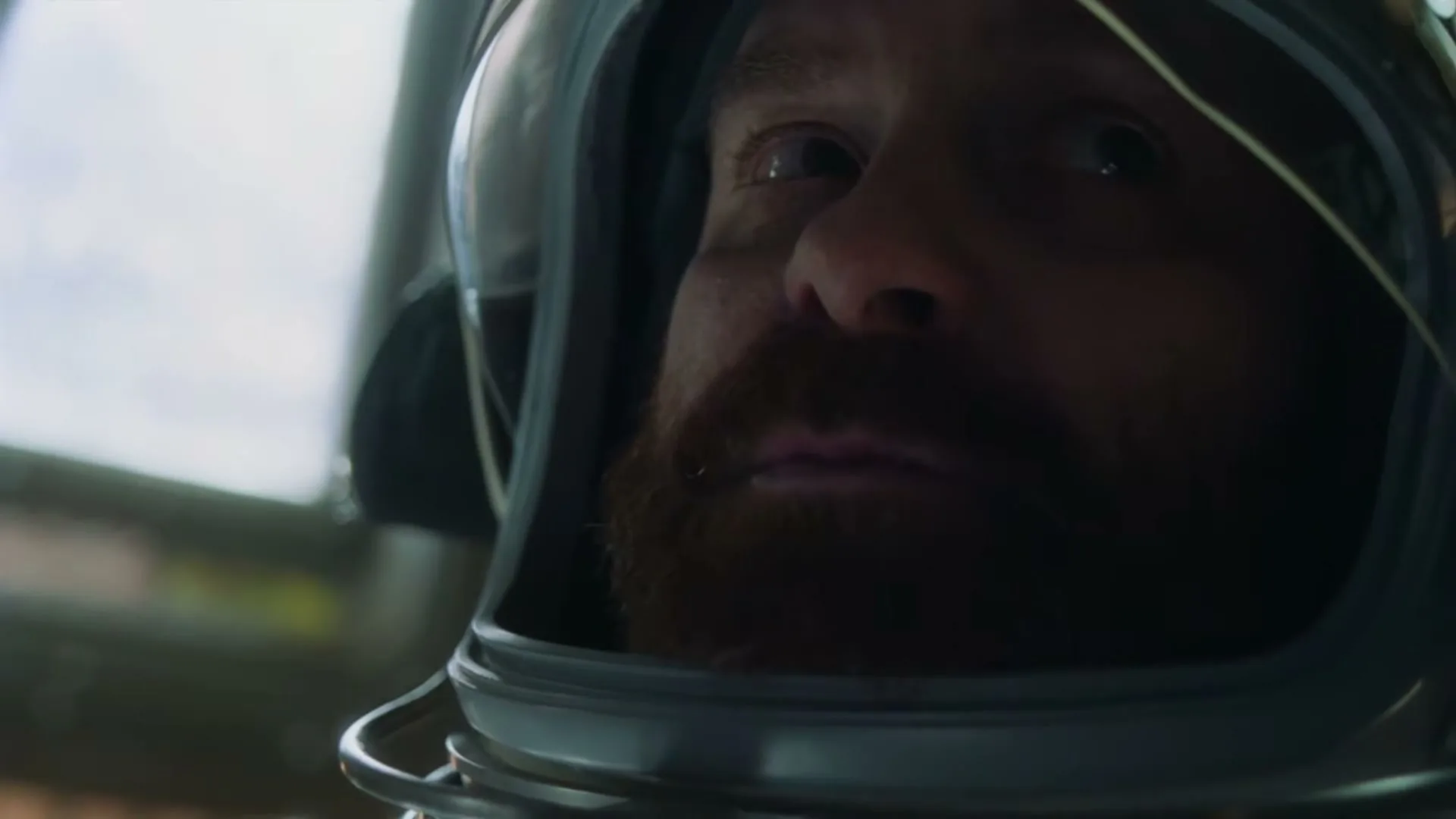 A red-bearded man in a space helmet looks up with a surprised expression, illuminated by light from above.