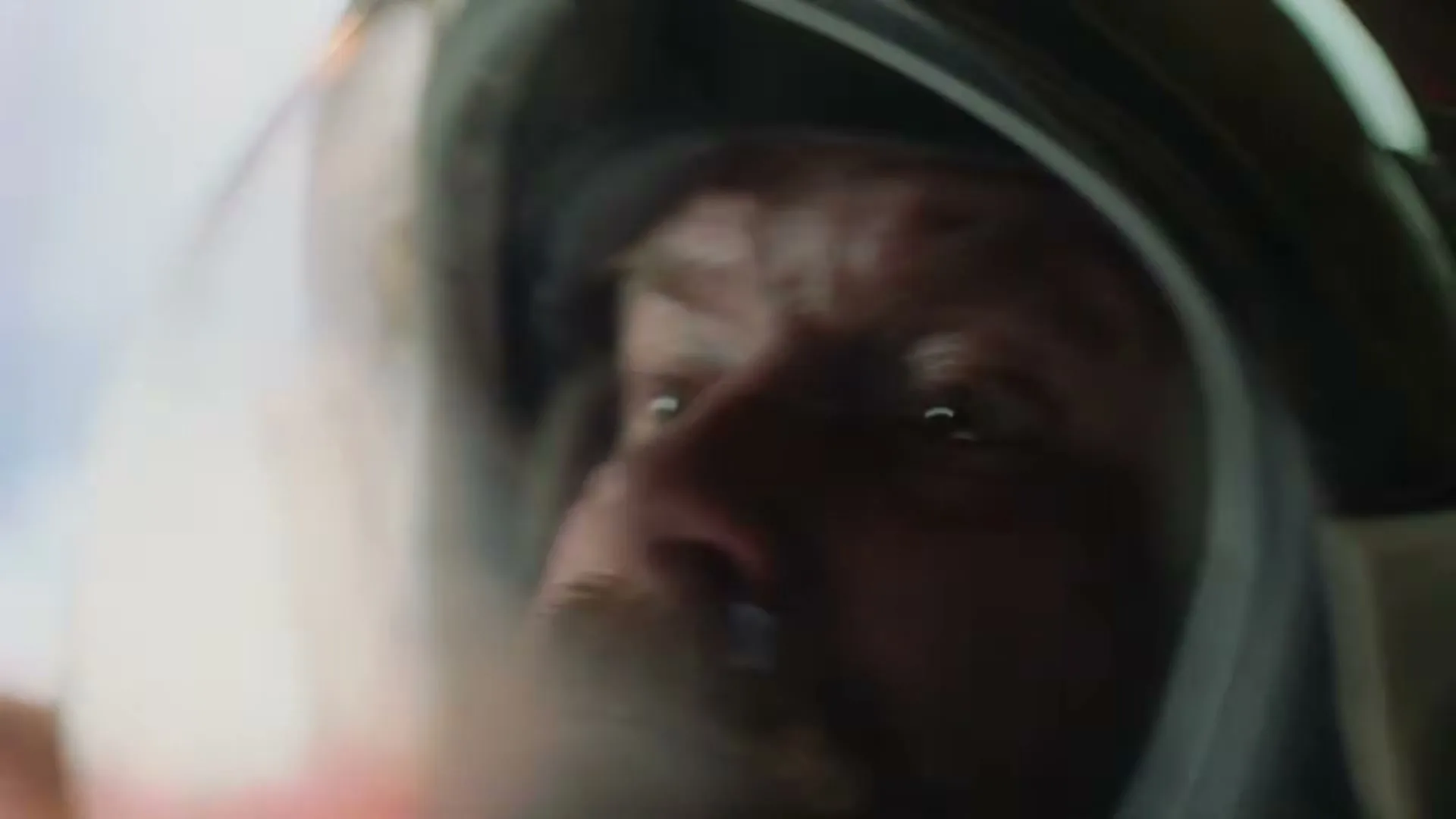 A man in his 30s, wearing a space helmet, looks up with a determined expression as he experiences turbulence in a spaceship.