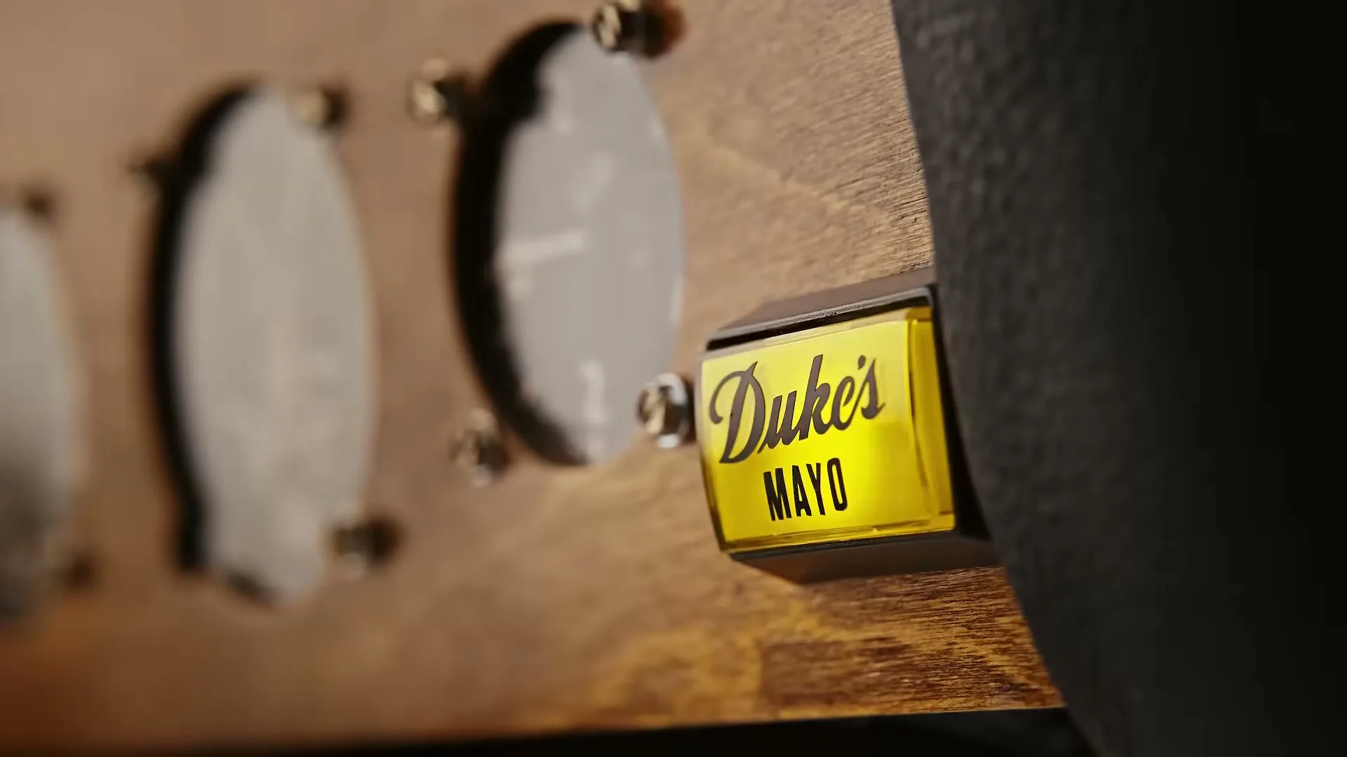 A close-up shot of a wooden panel with gauges and a yellow "Duke's Mayo" button, suggesting a vintage or custom-built device.