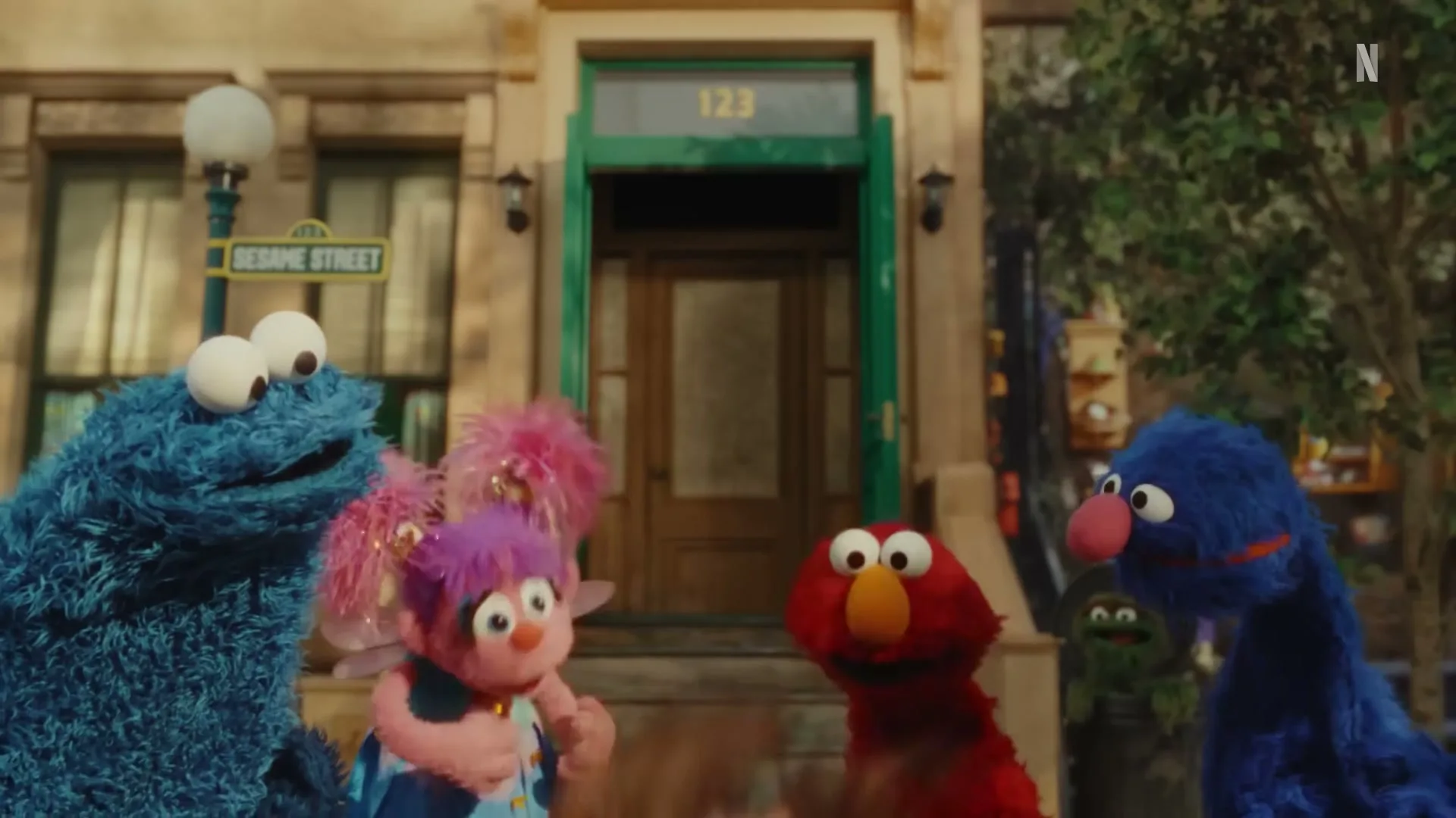 A young woman puppet with brown hair and a denim jacket is surrounded by Cookie Monster, Elmo, Grover, and Abby Cadabby on Sesame Street.