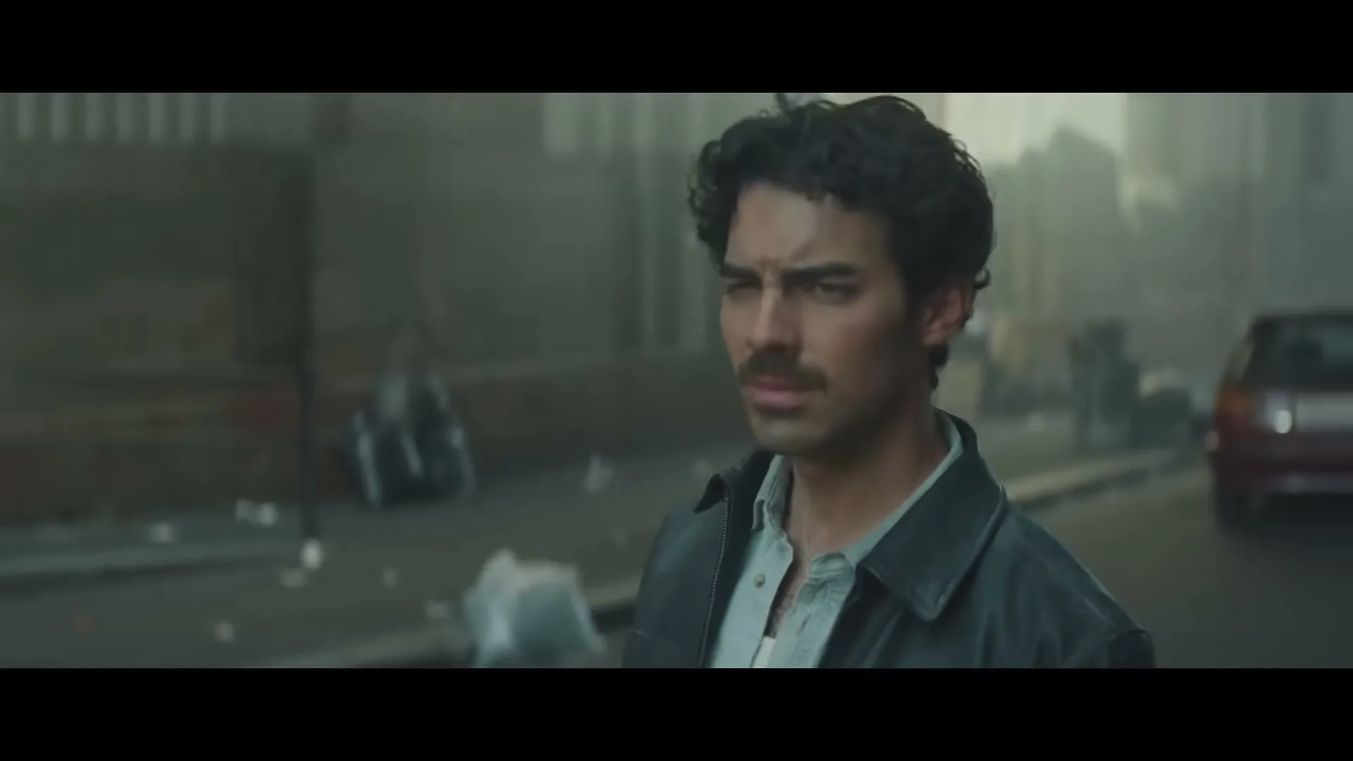 A man with a mustache and curly hair looks around a dusty, deserted city street.