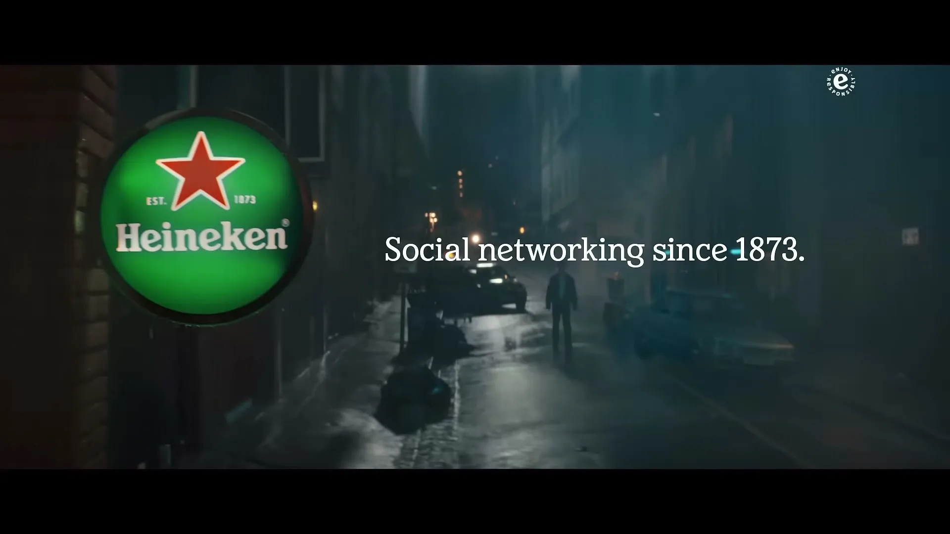 A man walks down a dark, wet alley at night, with a glowing Heineken sign on the left and text overlayed on the right.