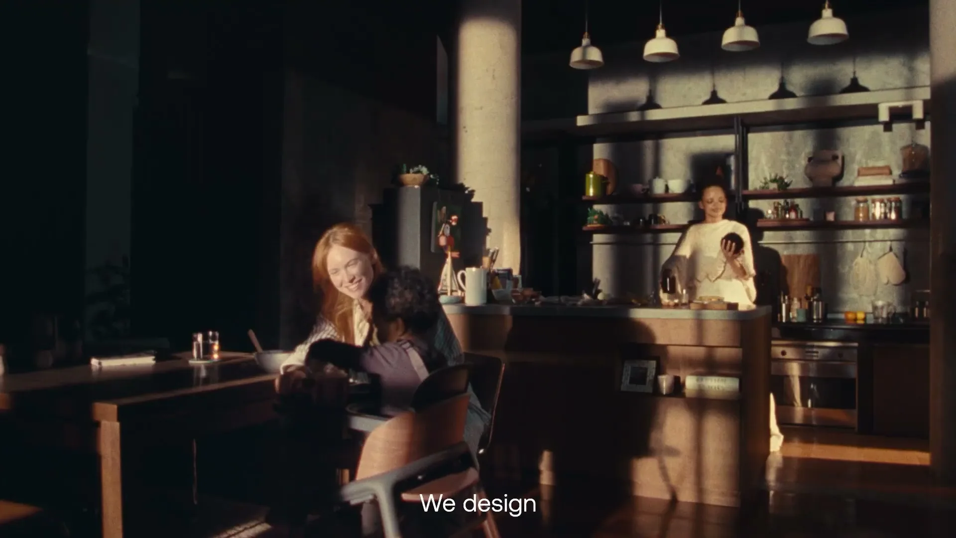 A diverse family in a modern kitchen, with a mother and child at a table and another woman cooking in the background, bathed in warm sunlight.