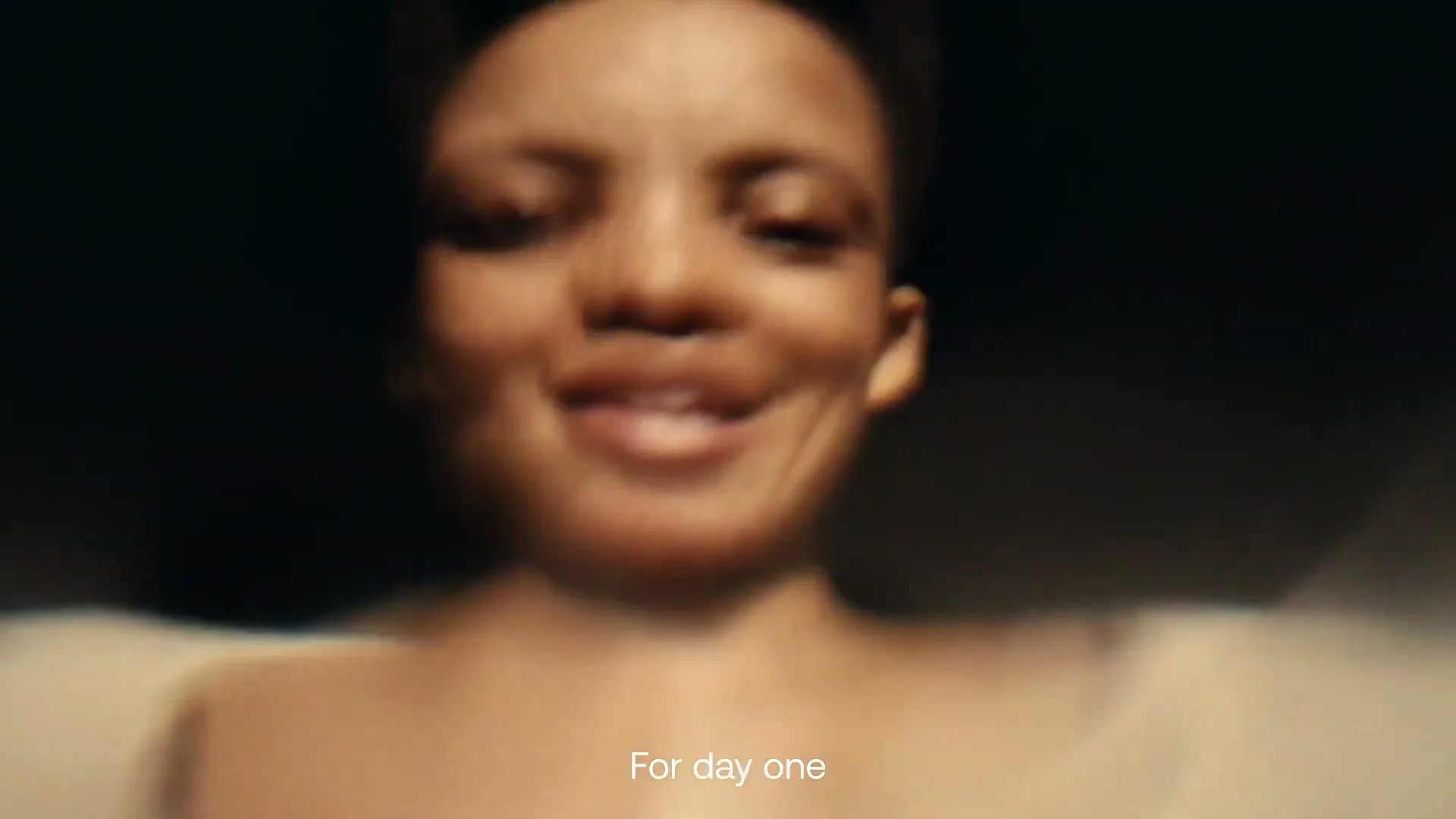 A blurry, smiling woman with short hair looks down at the camera, with the text "For day one" on screen.