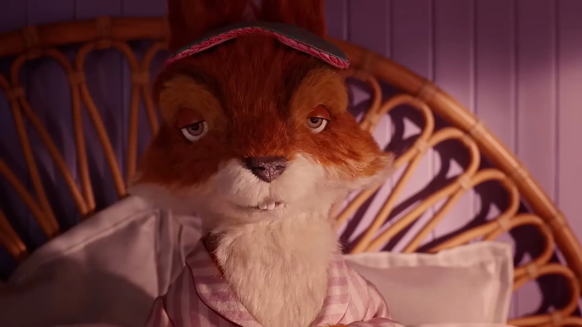 A stop-motion animated squirrel character, wearing a sleep mask and pajamas, wakes up in bed, looking around with sleepy eyes in a bedroom.