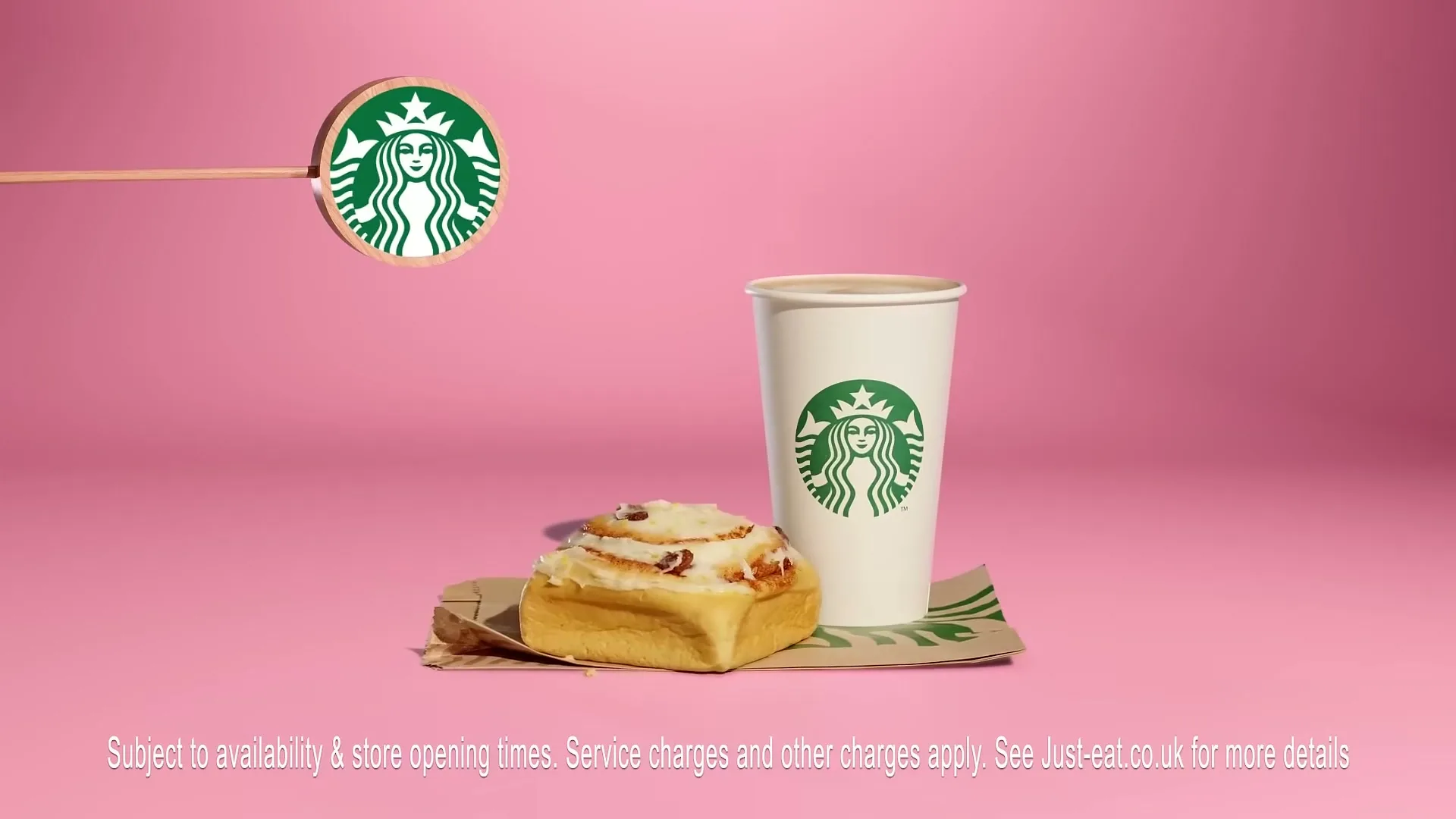 A McDonald's breakfast sandwich, hash brown, and coffee cup are displayed on a pink surface, with a McDonald's logo on a stick.
