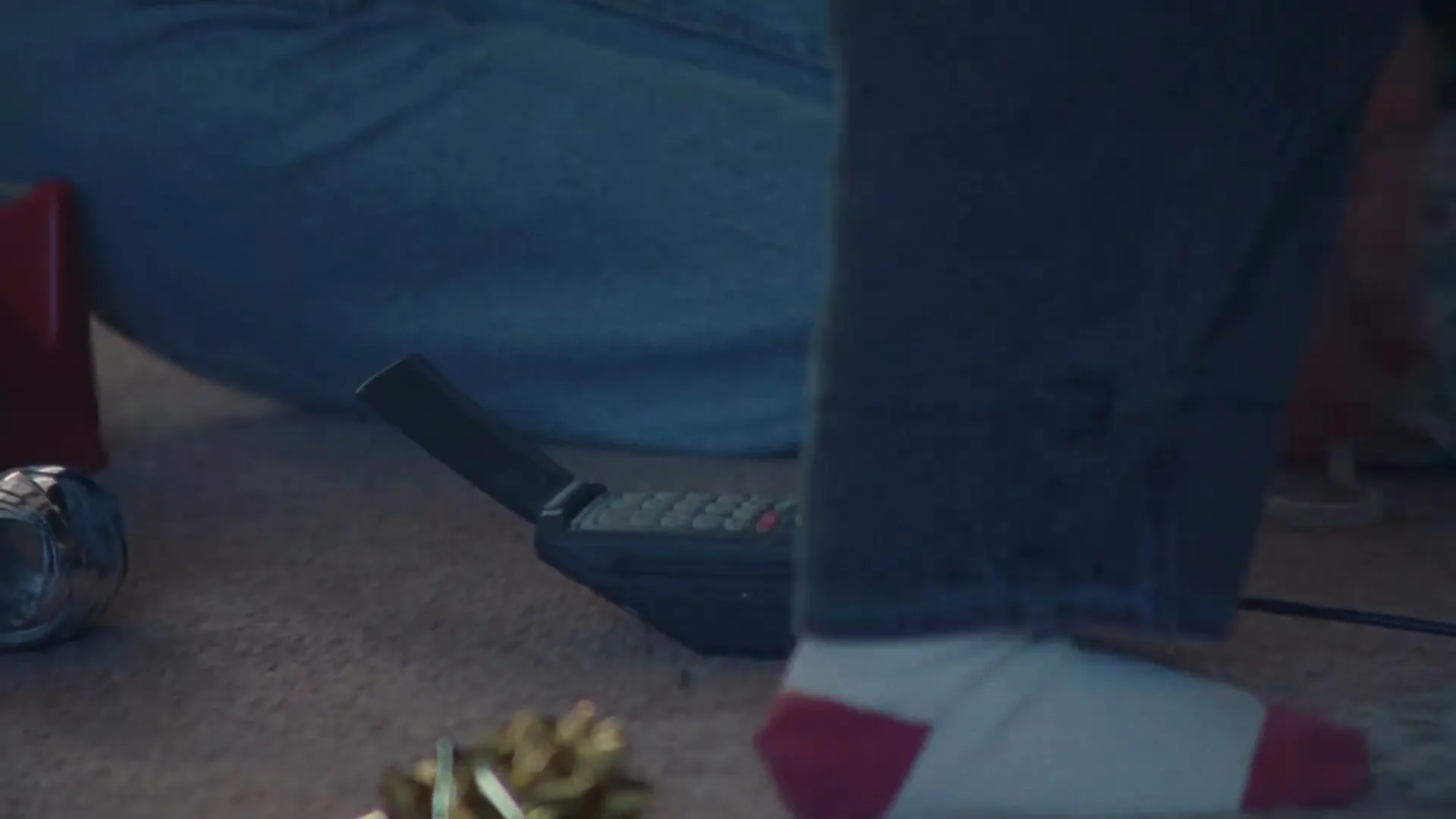 A person in jeans and red-and-white socks walks past an old-fashioned mobile phone on a carpeted floor, with Christmas decorations nearby.