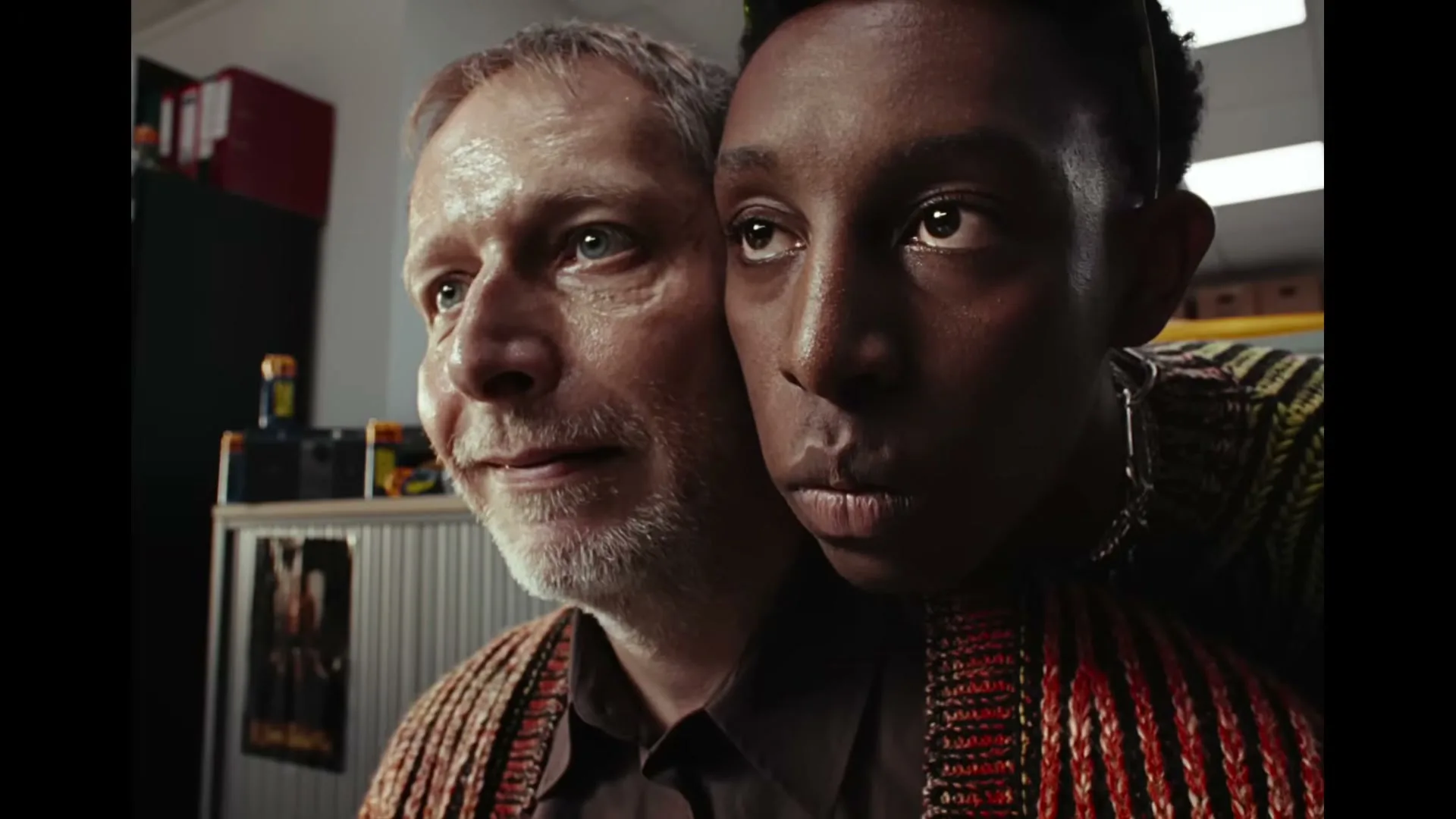 A young Black man and an older white man are fused together, looking in different directions in an office setting.
