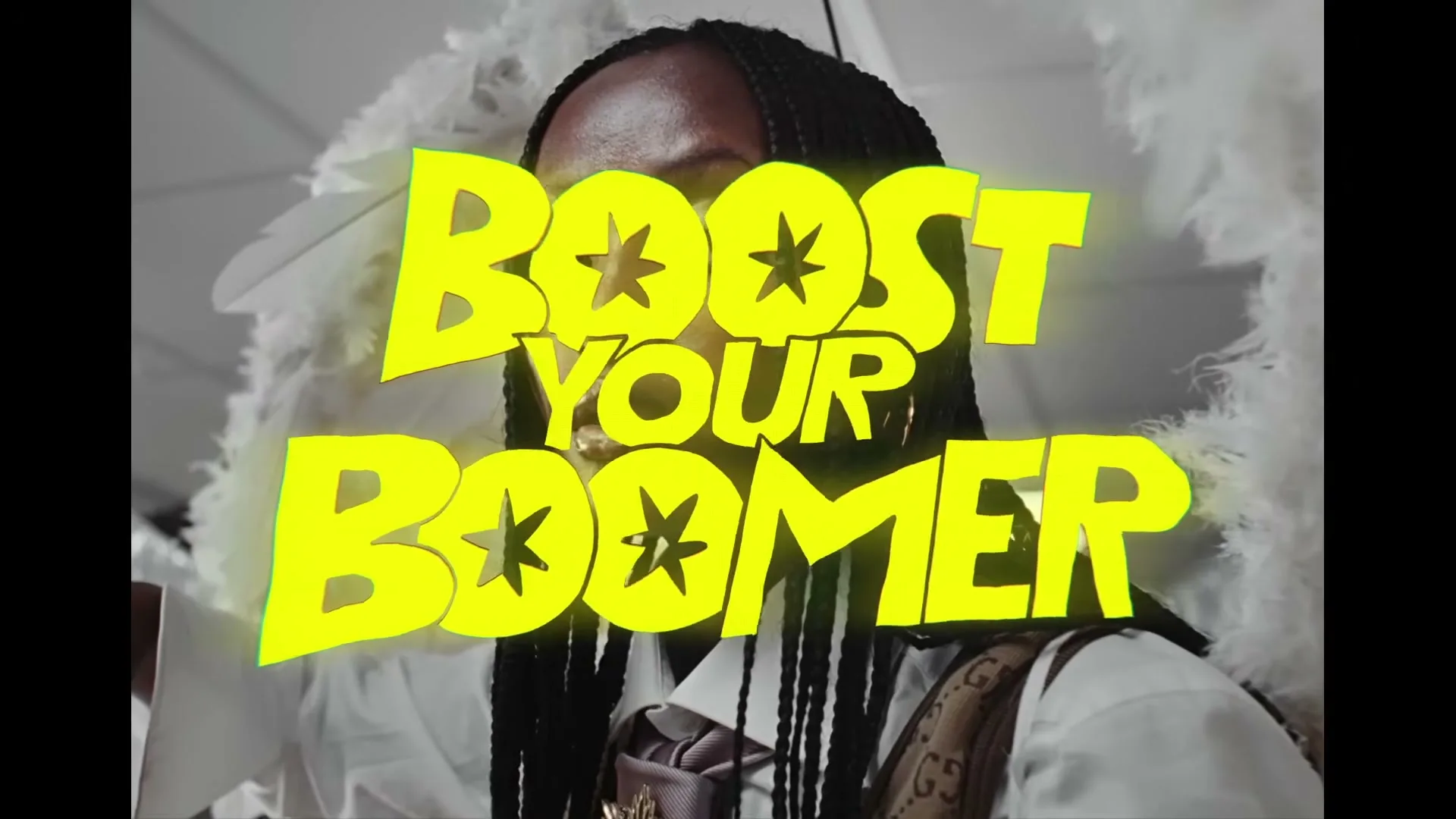 A person with braided hair and white angel wings wears a white shirt and tie, with "BOOST YOUR BOOMER" text overlayed, in an interior setting.