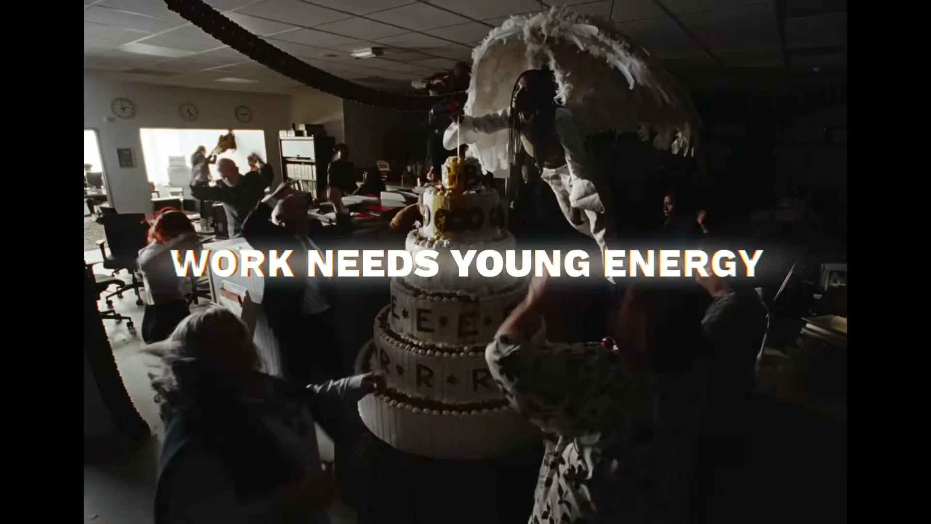A diverse group of office workers dance around a giant cake, while a person with large white wings stands atop it, in a chaotic office party.