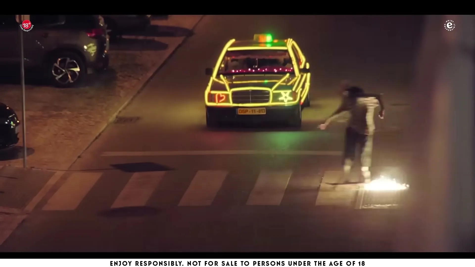 A man and woman dance in front of a taxi decorated with neon lights and sparklers on a street at night.