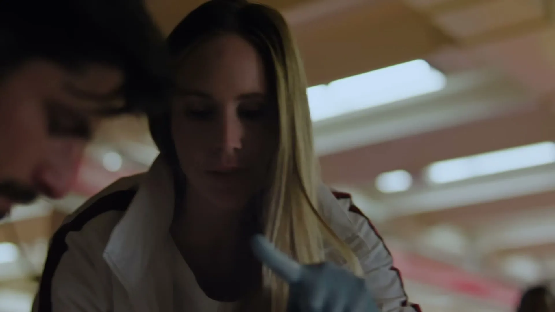 A female medical professional in a white jacket and blue gloves examines a male patient's eyes in a dimly lit room.