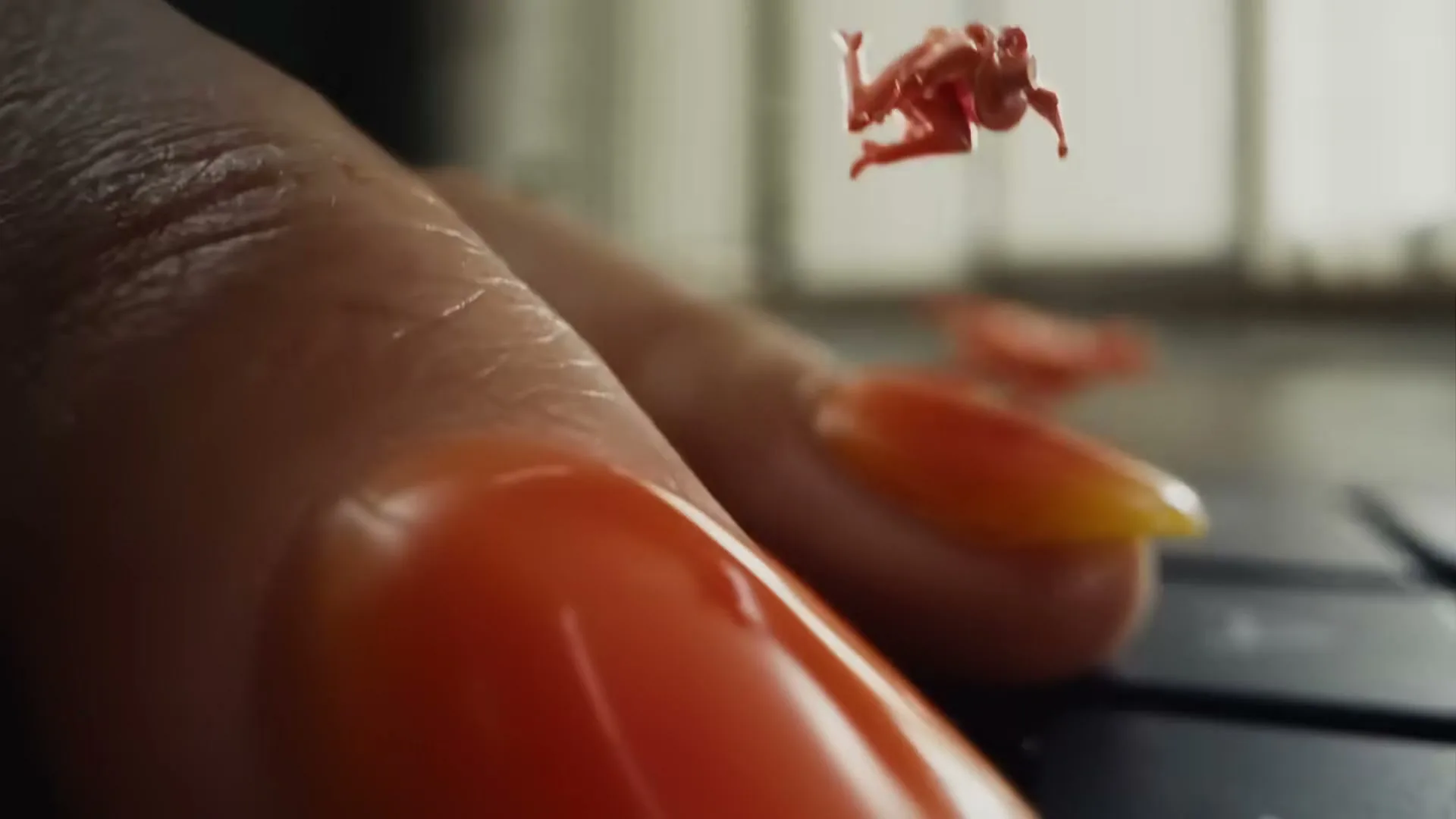 A tiny orange cowboy figurine on a horse jumps from a woman's fingernail onto a laptop keyboard, then another cowboy appears.
