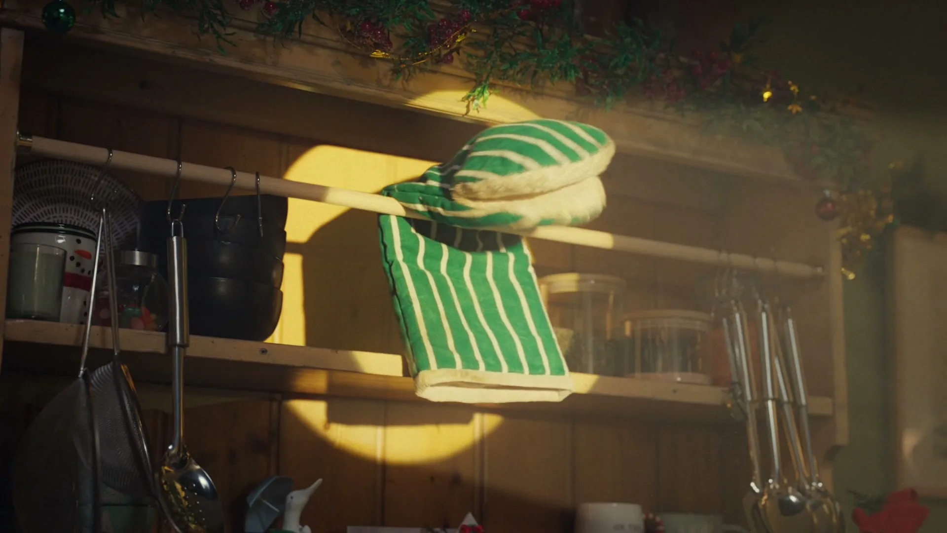 A green and white striped oven mitt and towel hang on a wooden rack in a kitchen, illuminated by a warm spotlight.