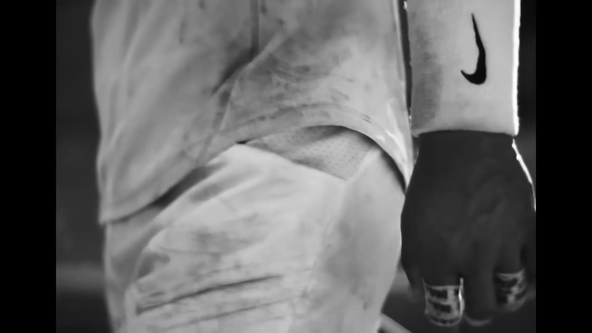 A close-up shot of a person's hand and torso, wearing a white athletic sleeve with a Nike logo and rings on their fingers, in a black and white setting.