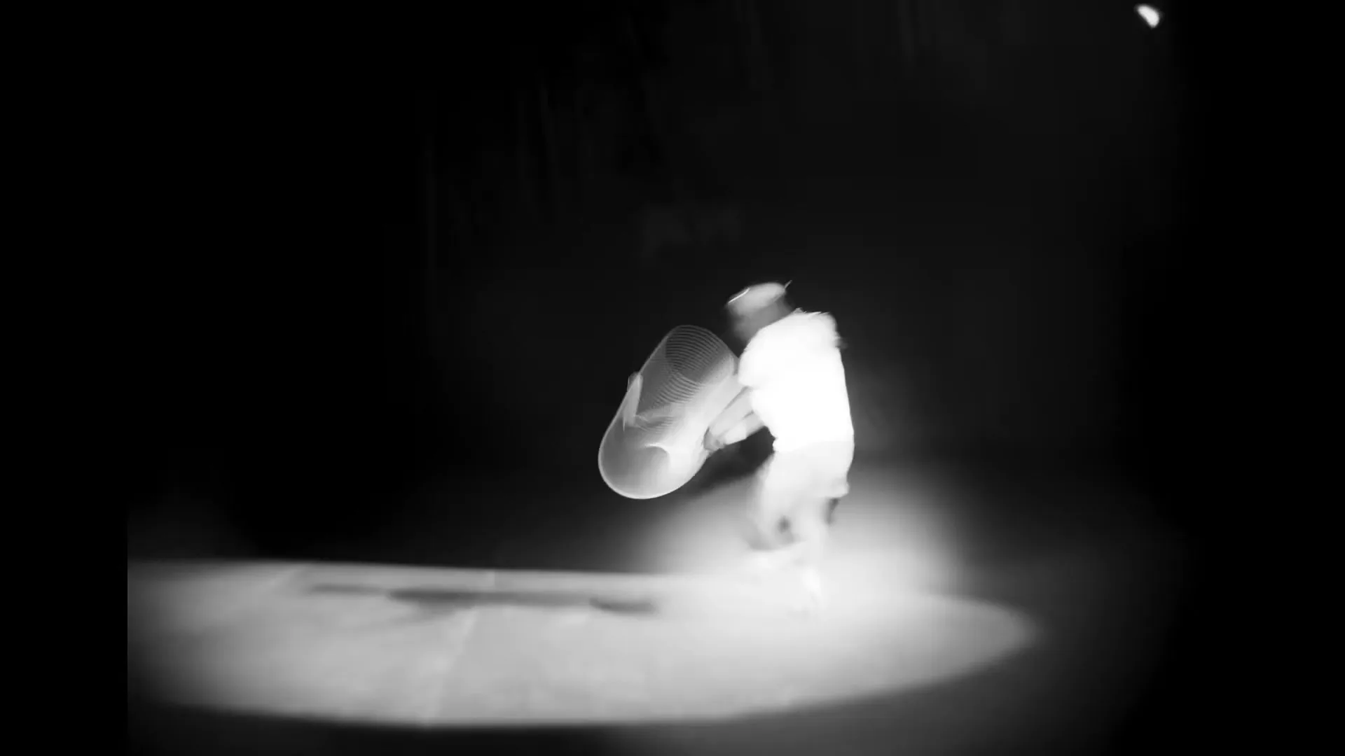 A tennis player in white attire is captured in a blurry, high-contrast black and white shot, hitting a tennis ball in a spotlight on a dark court.