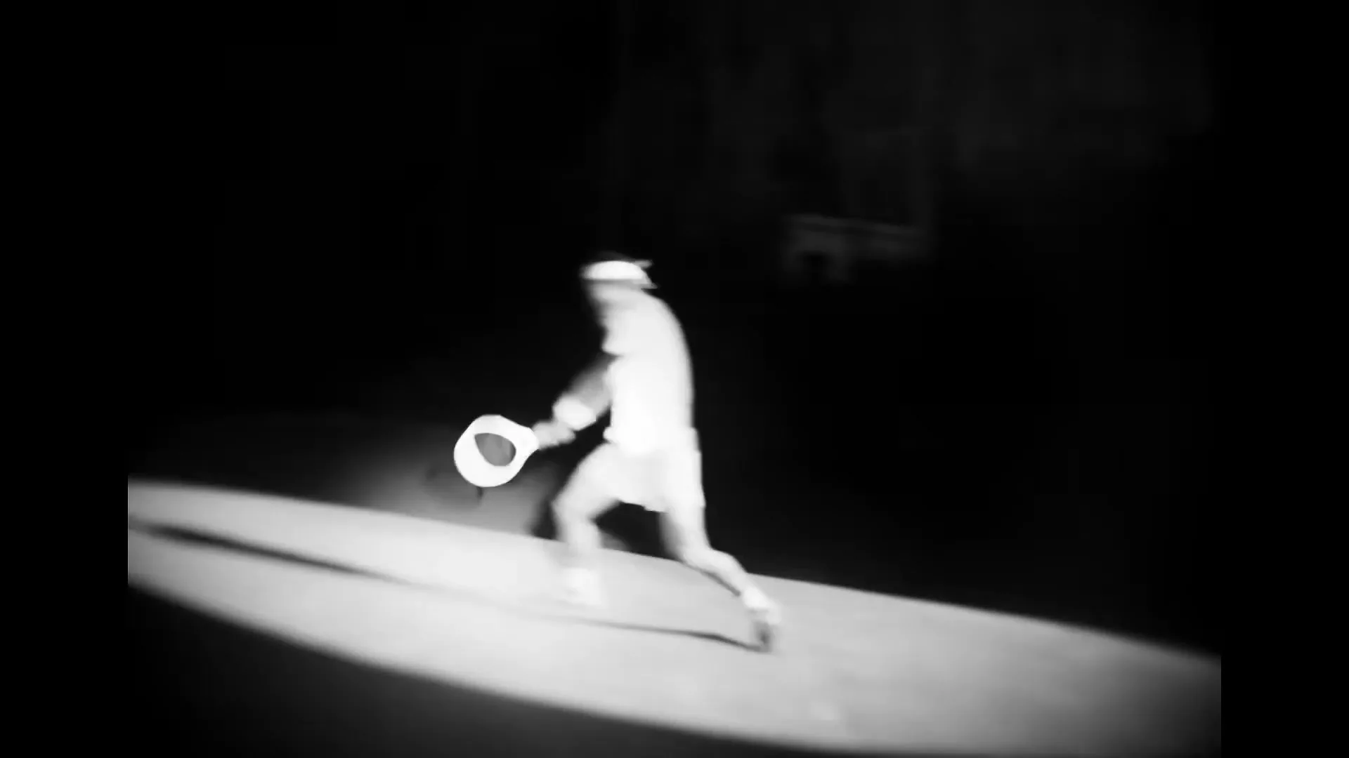 A tennis player in white sportswear, possibly Rafael Nadal, is captured in a blurry, high-contrast black and white shot, mid-swing on a dimly lit court.