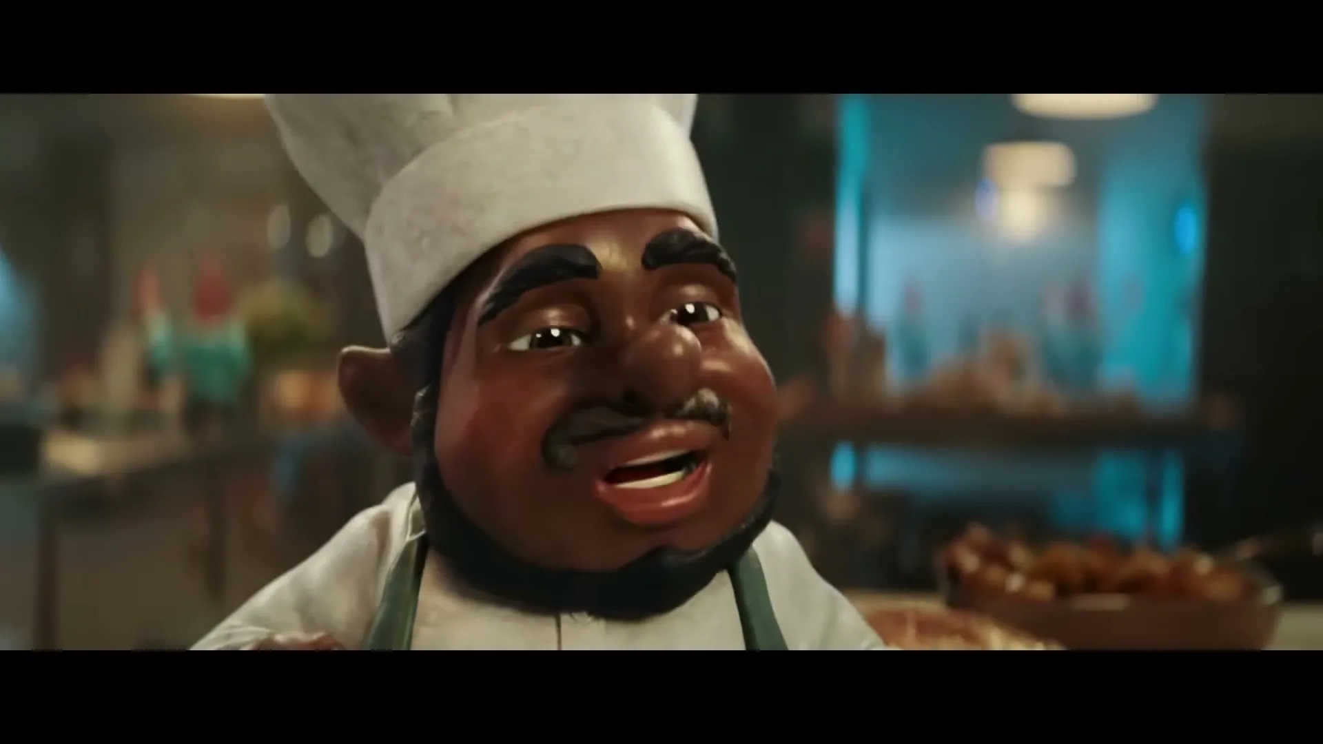 A CGI animated male chef gnome with dark skin and a white chef's hat smiles and gestures with his hands in a kitchen.