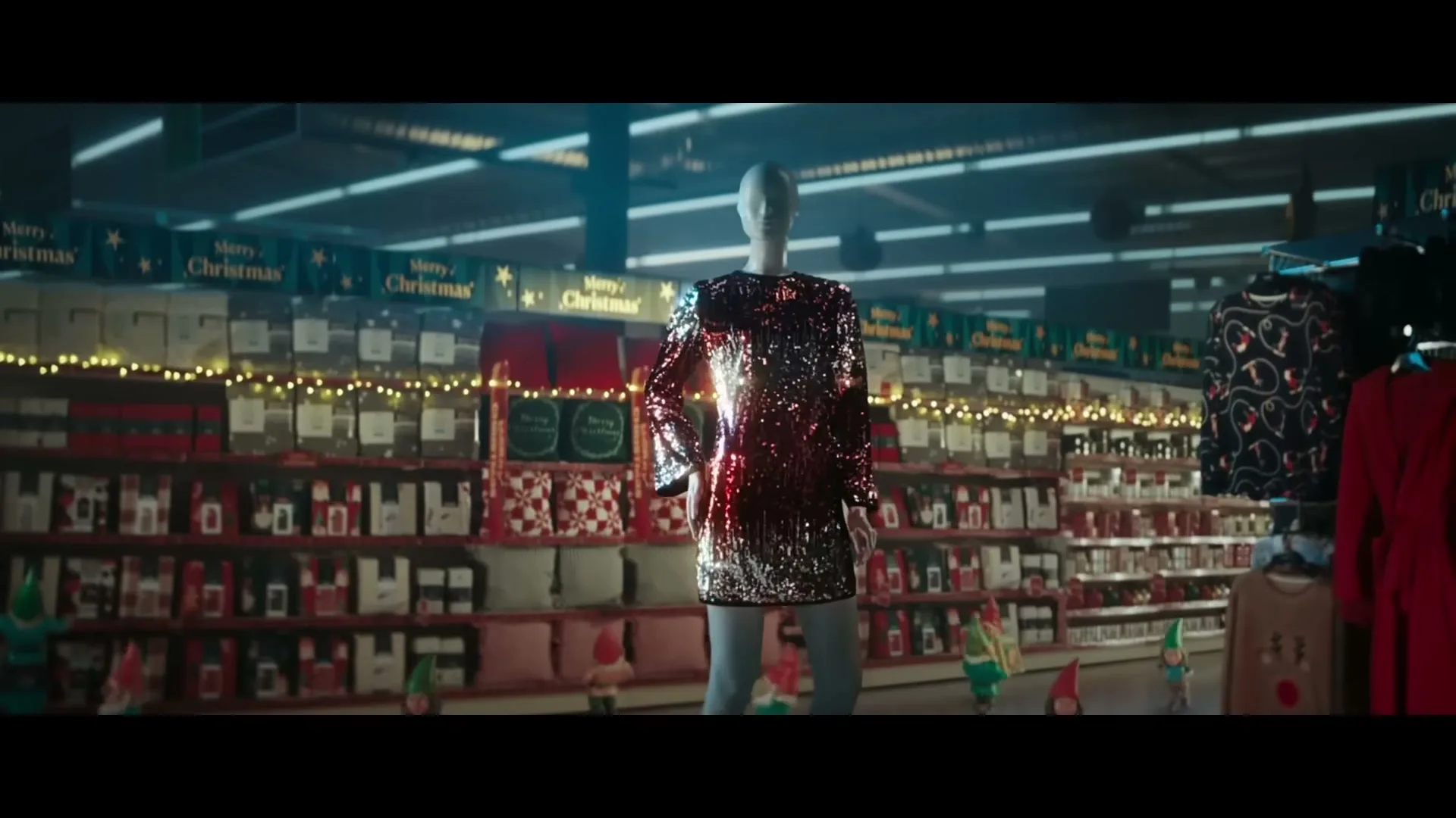 A mannequin wearing a sparkly red and silver dress stands in the middle of a supermarket aisle decorated for Christmas, surrounded by shelves of products.
