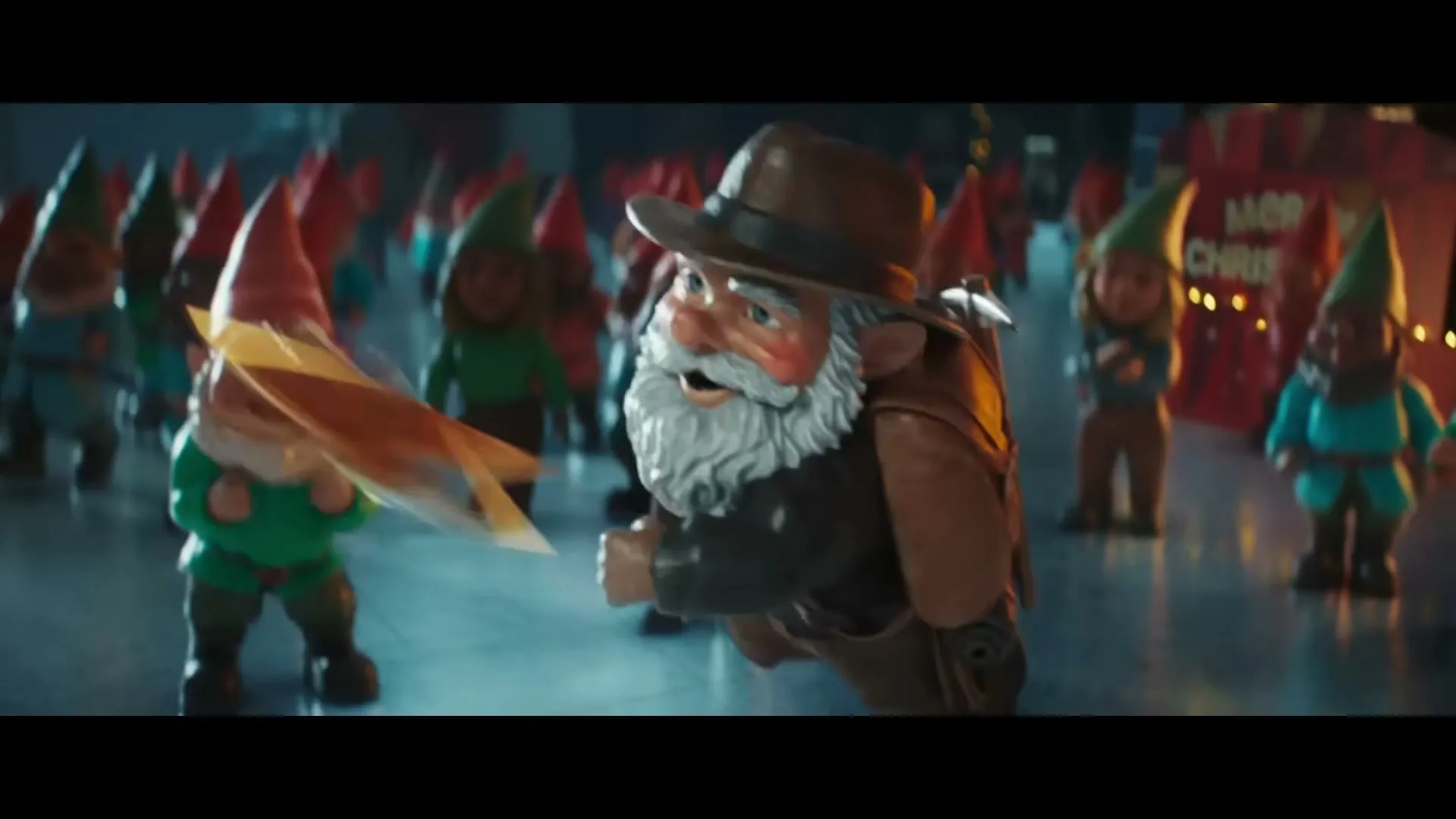 A male gnome with a white beard and brown hat holds a golden star, surrounded by many other gnomes in a large, open space.