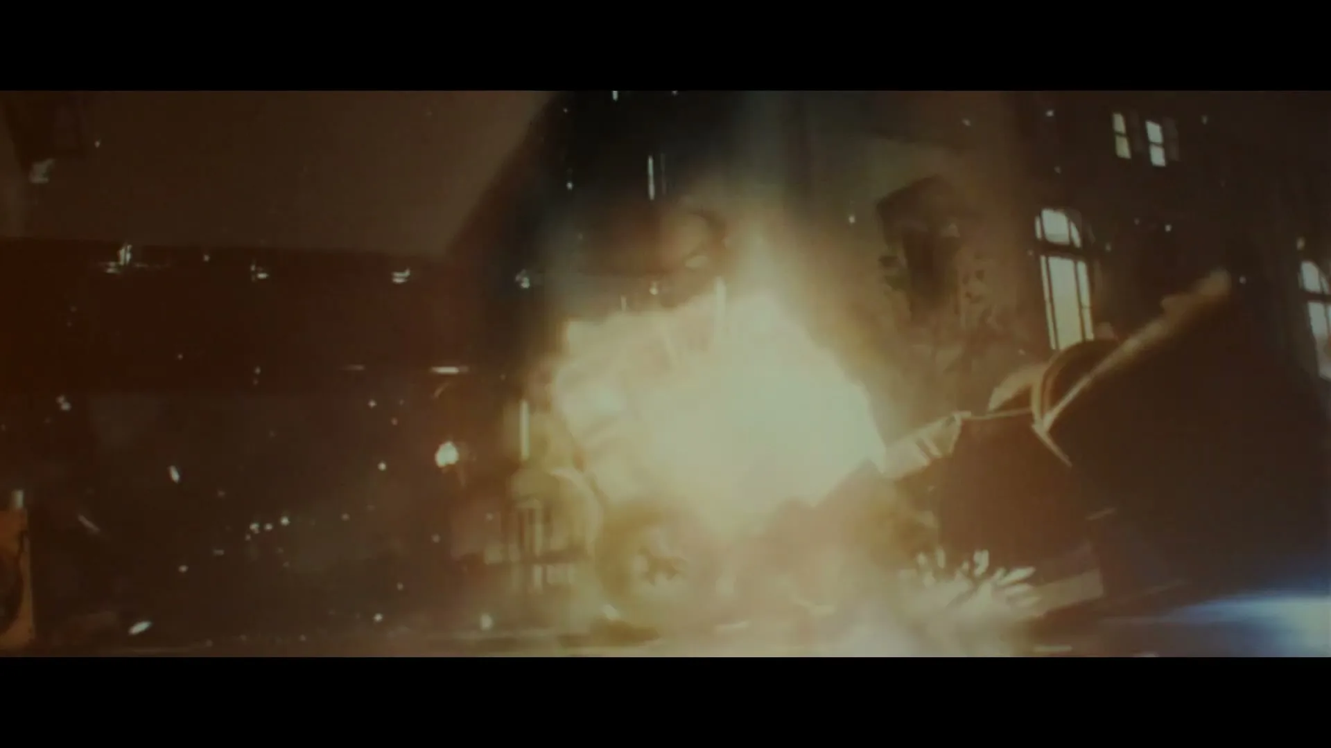 A car explodes in a fiery crash on a city street at night, with debris flying everywhere and buildings in the background.