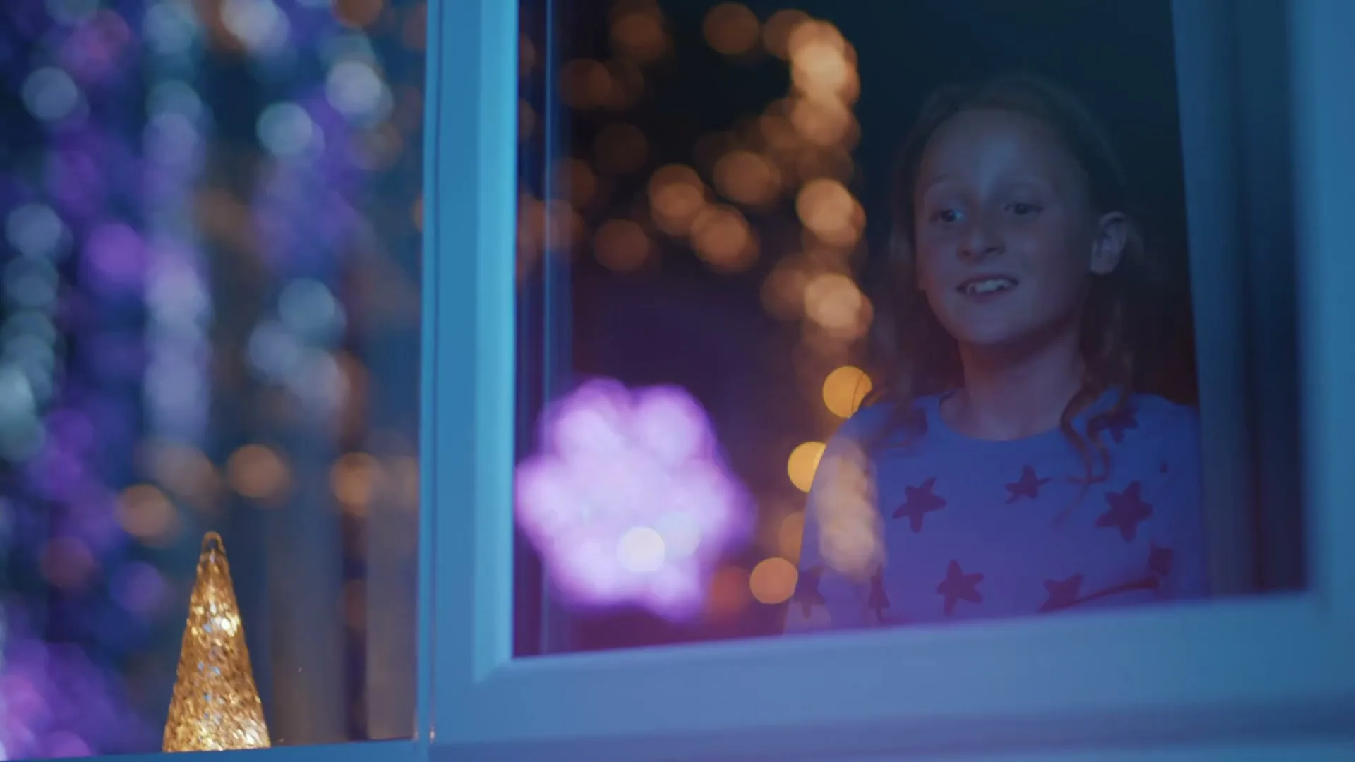 A young girl with red hair looks out a window at night, with colorful bokeh lights in the background.