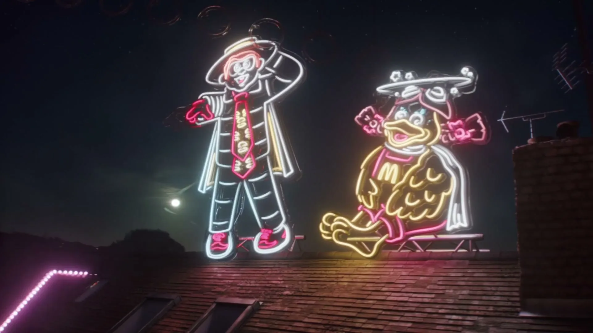 Two neon McDonald's characters, a man and a duck, are displayed on a rooftop at night, glowing brightly against the dark sky.