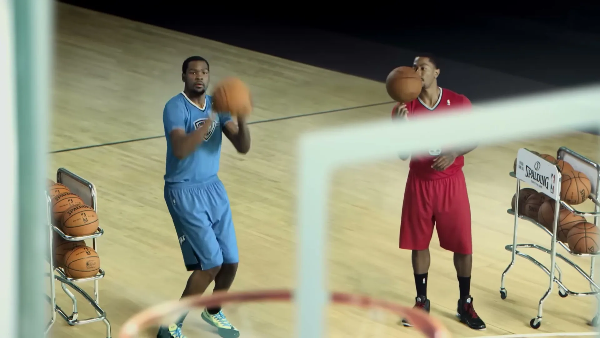 Two male basketball players, one in blue and one in red, stand on a basketball court, dribbling and shooting a basketball.