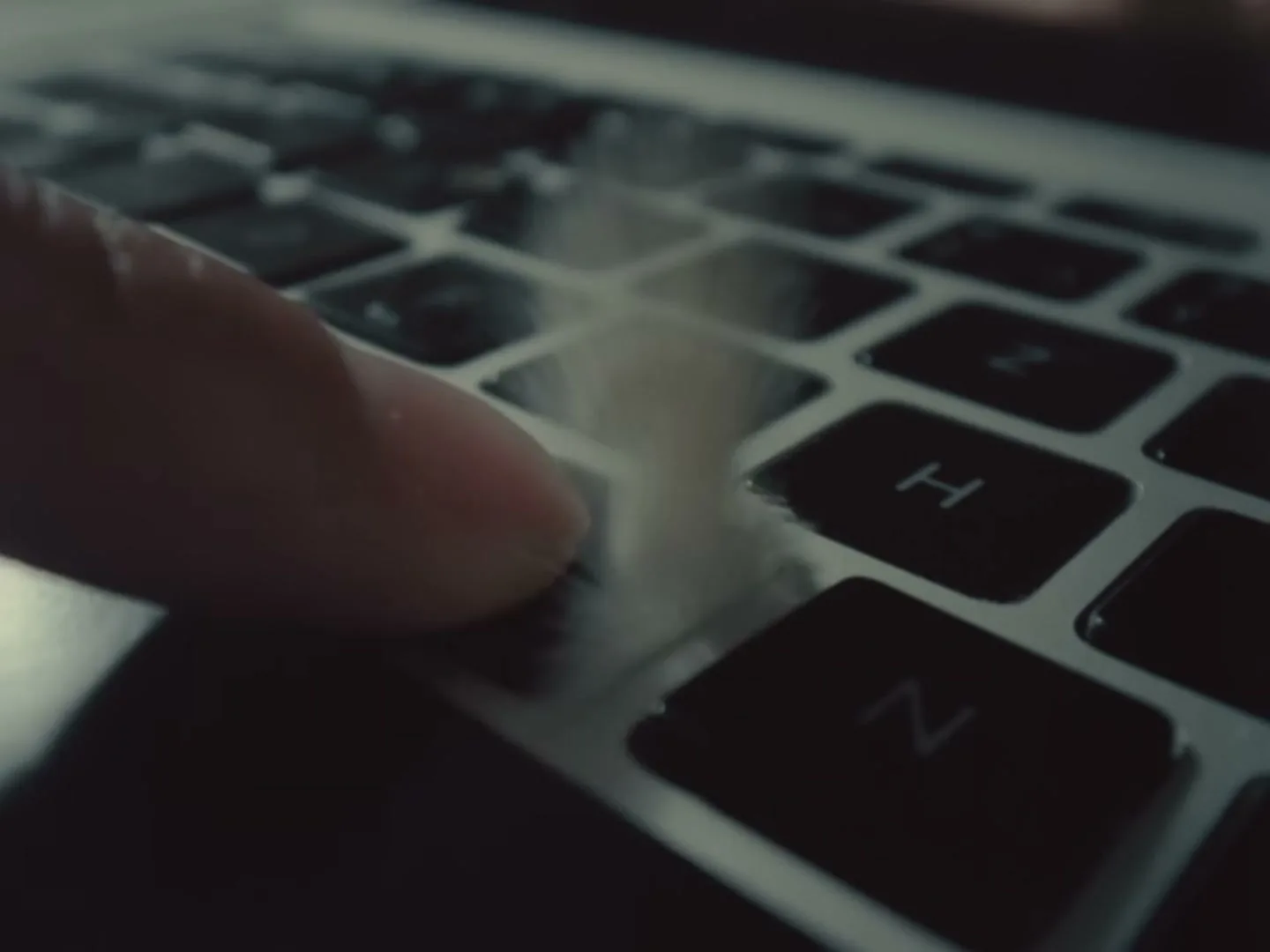 A finger presses the 'F' key on a laptop keyboard, causing white sugar to explode from beneath the key, in a close-up shot.