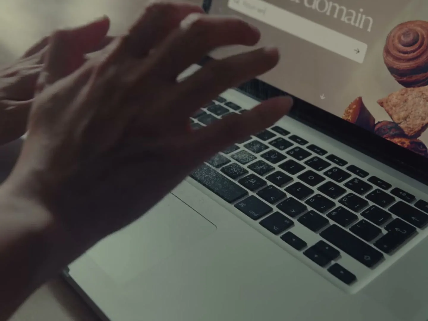 A person's hands hover over a laptop keyboard, with a website showing bakery items on the screen.