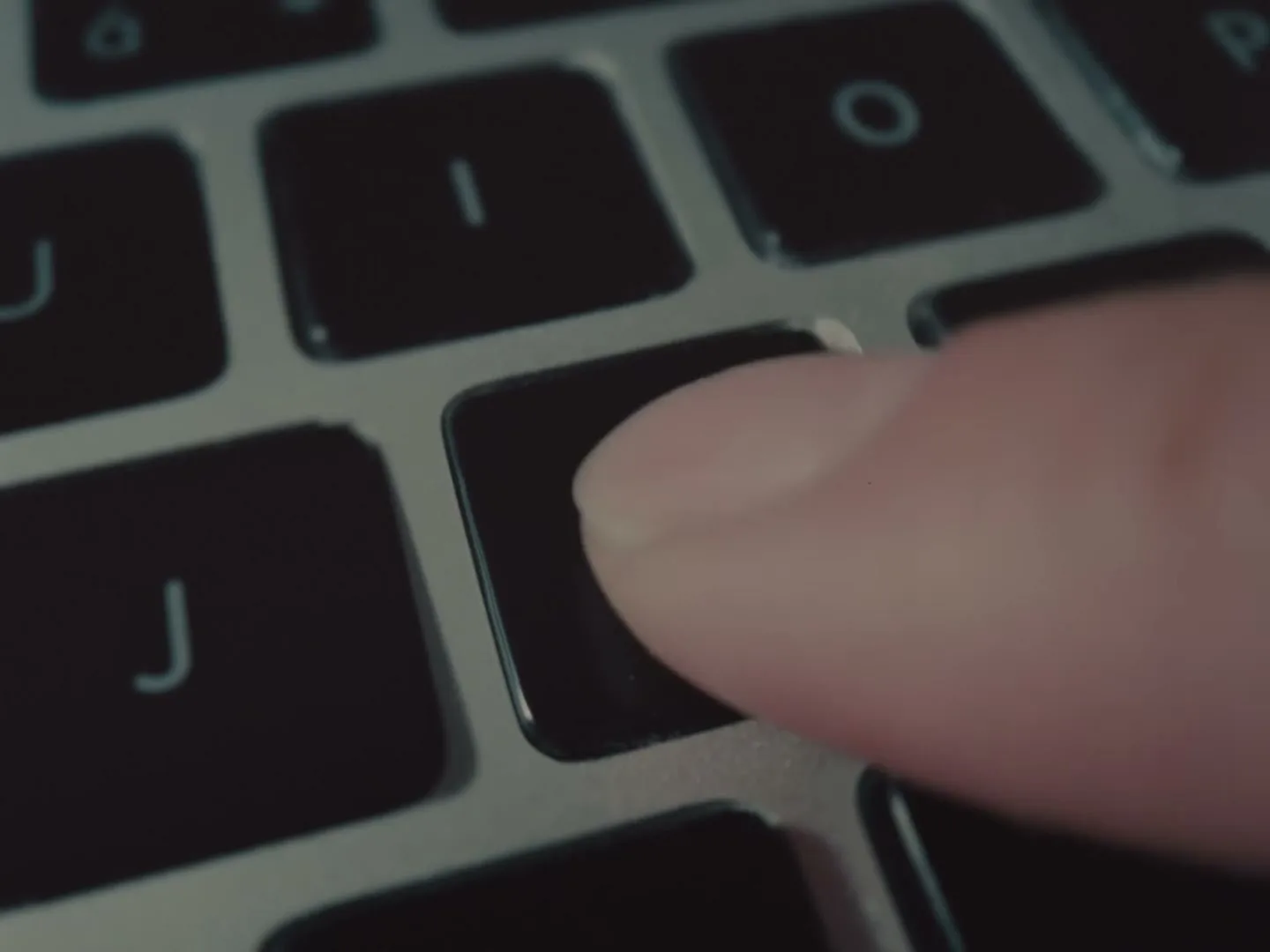 A close-up shot shows a finger pressing the 'M' key on a laptop keyboard.