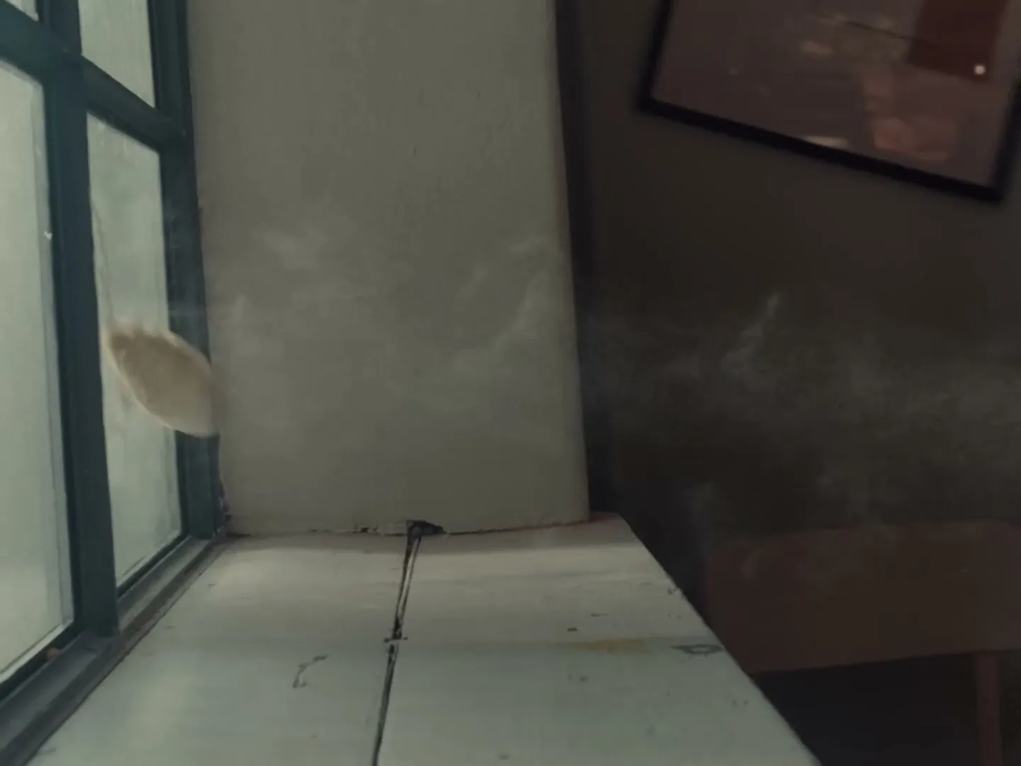 A small, light-colored pastry is thrown and lands on a white windowsill next to a window in an interior setting.