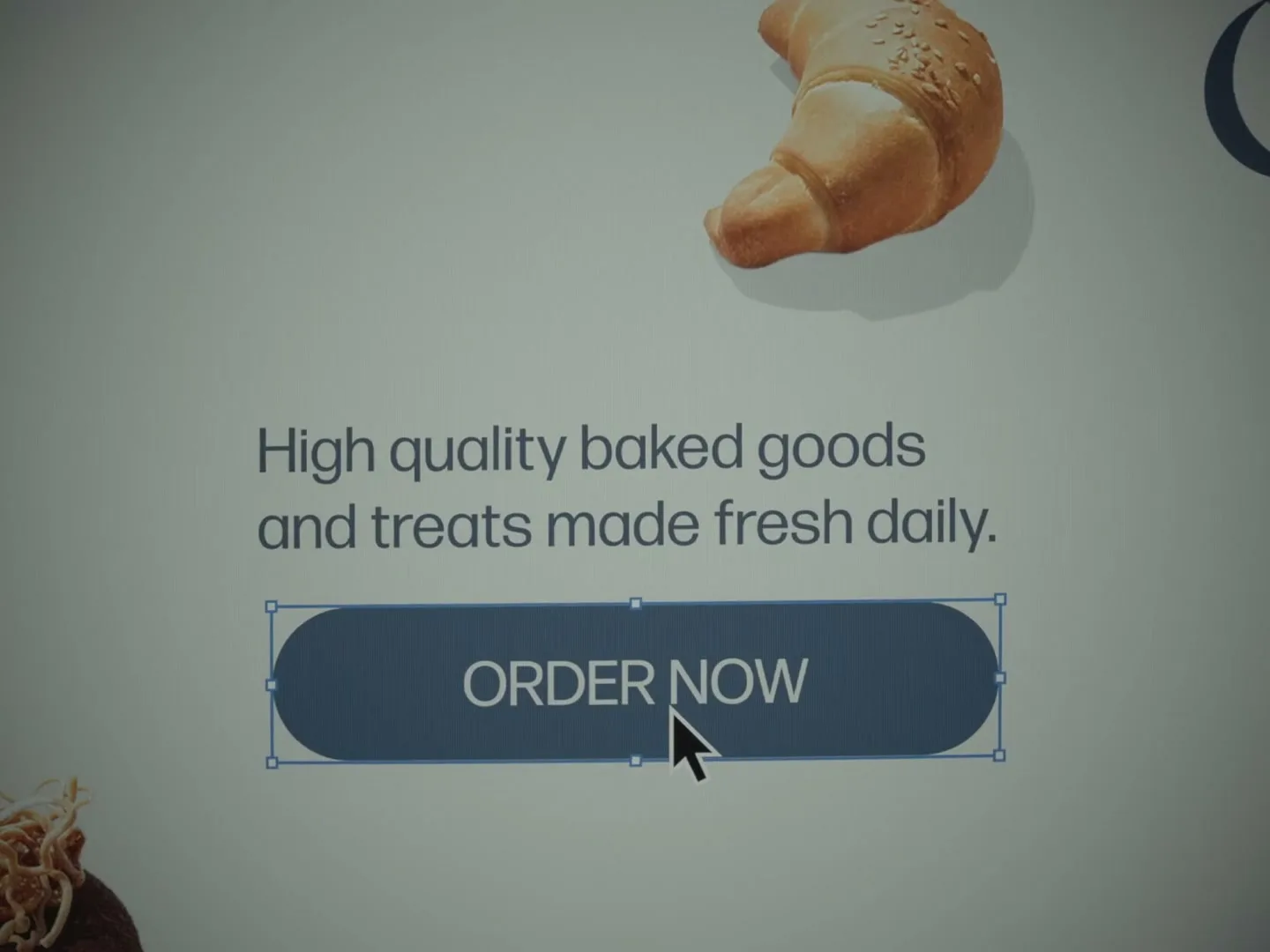 A close-up shot of a computer screen shows a website design with a croissant image and text, as a cursor hovers over an "ORDER NOW" button.
