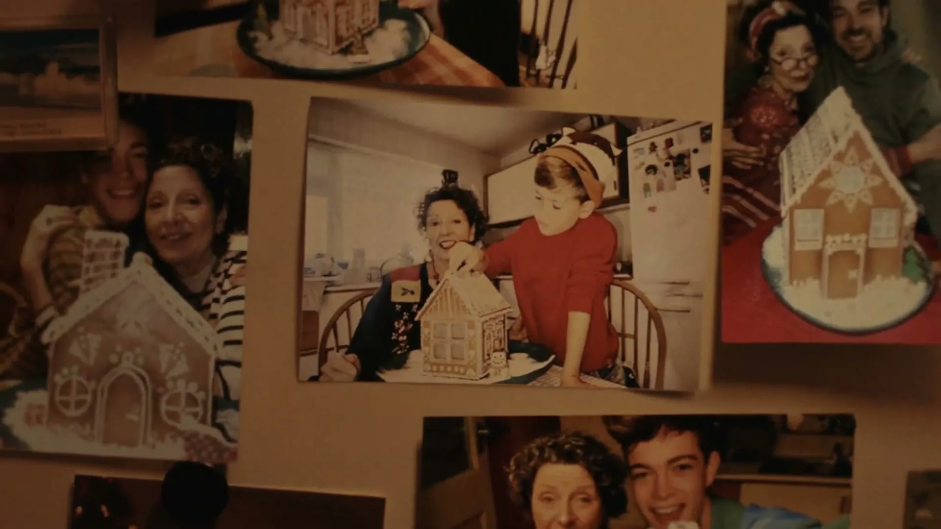 A young man looks at old photos of his family making gingerbread houses, then an older man decorates a gingerbread house in a kitchen.