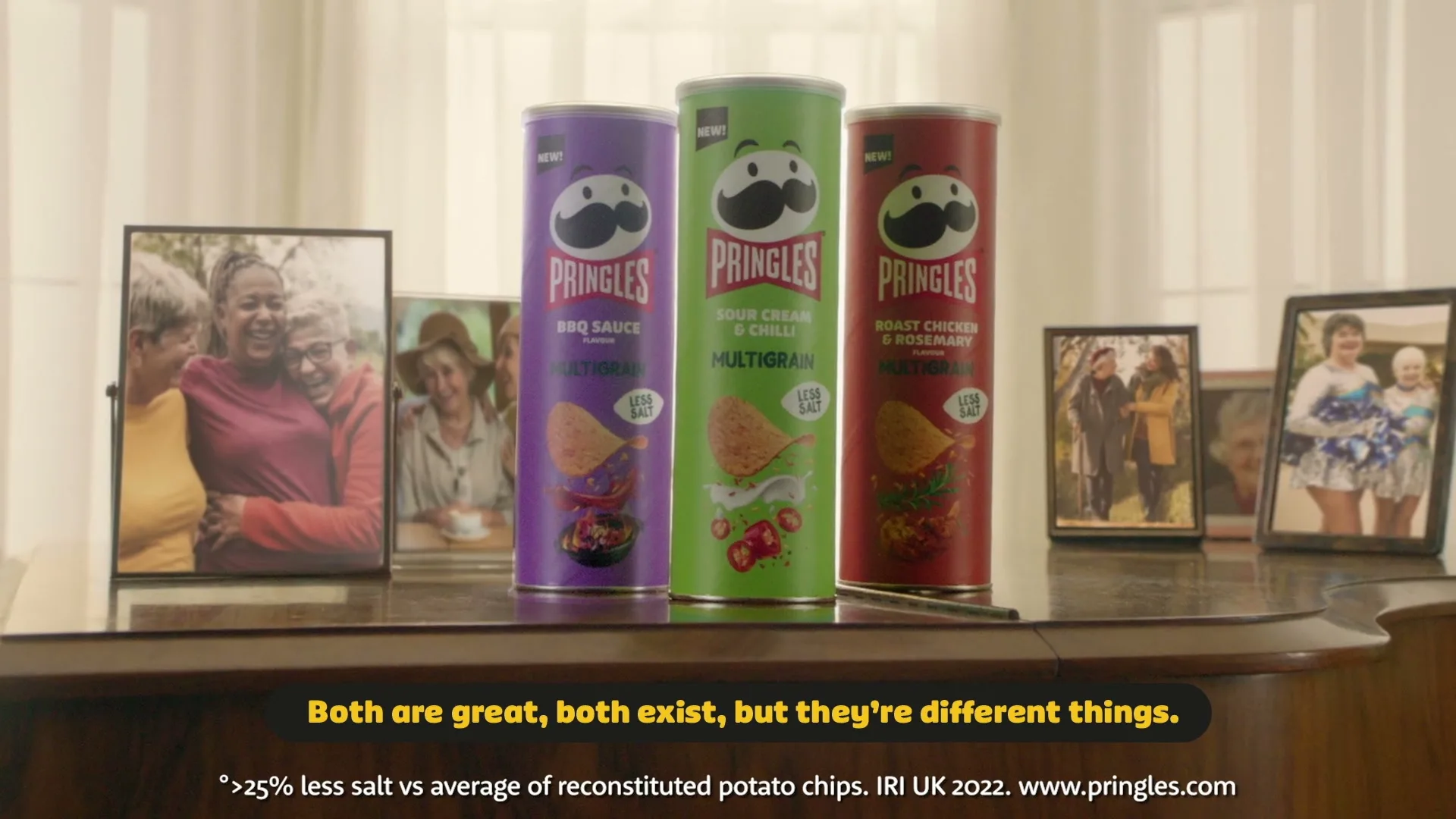 Three Pringles Multigrain cans stand on a wooden piano, surrounded by framed photos of diverse people, in a brightly lit room.