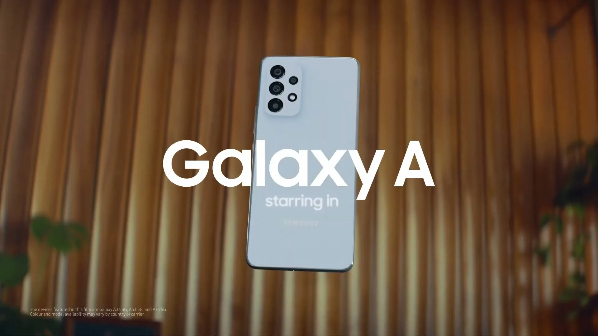 A black Samsung Galaxy A phone rotates and changes to white, with text appearing over it, against a blurred wooden background.