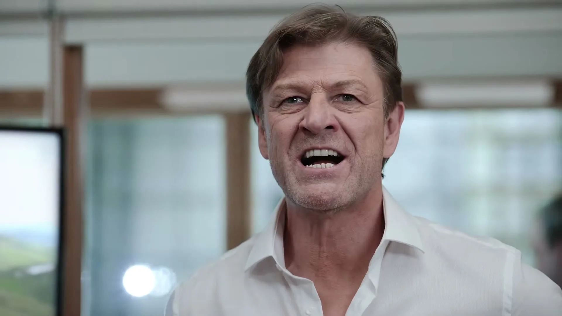 A man in his 60s, wearing a white shirt, drinks from a red Yorkshire Tea mug, then smiles and speaks in an office setting.