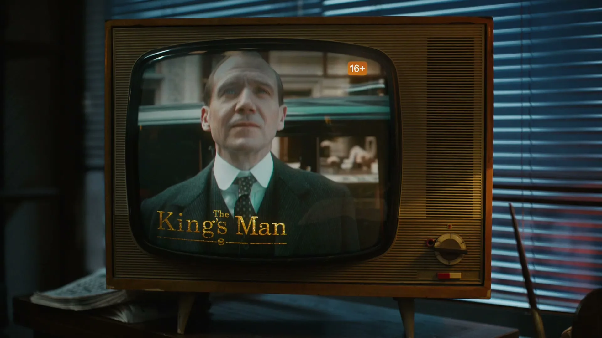 A man in a suit is shown on an old television set, with the title "The King's Man" on the screen, in a dimly lit room.