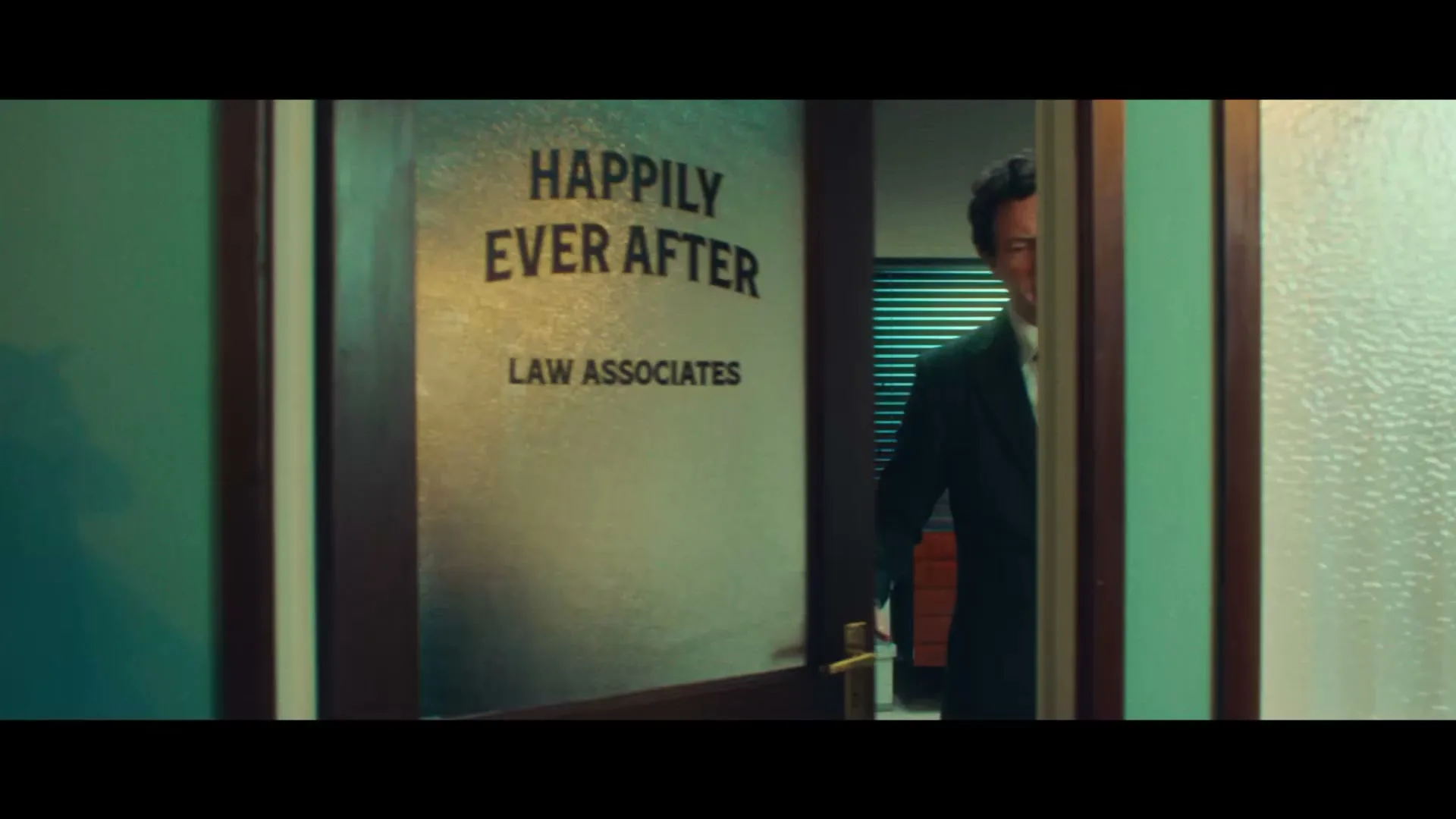 A man in a suit and headset stands in an office, then the shot transitions to a title card with text and a logo.