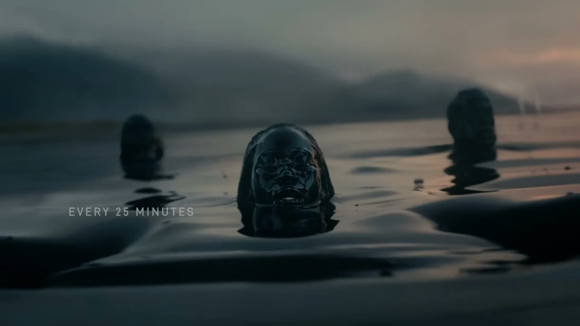 A woman covered in black oil emerges from dark water, with two other figures in the background, under a cloudy sky at dusk.