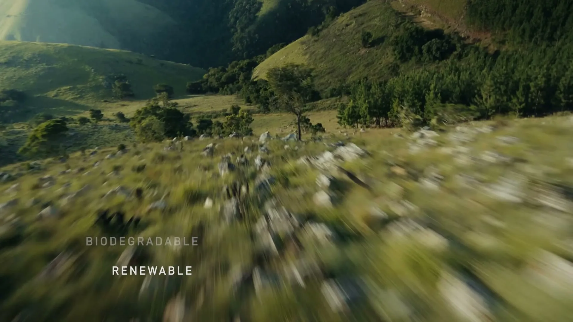 A wide, blurry shot of a green, rocky hillside with trees and valleys in the background, with text overlayed.