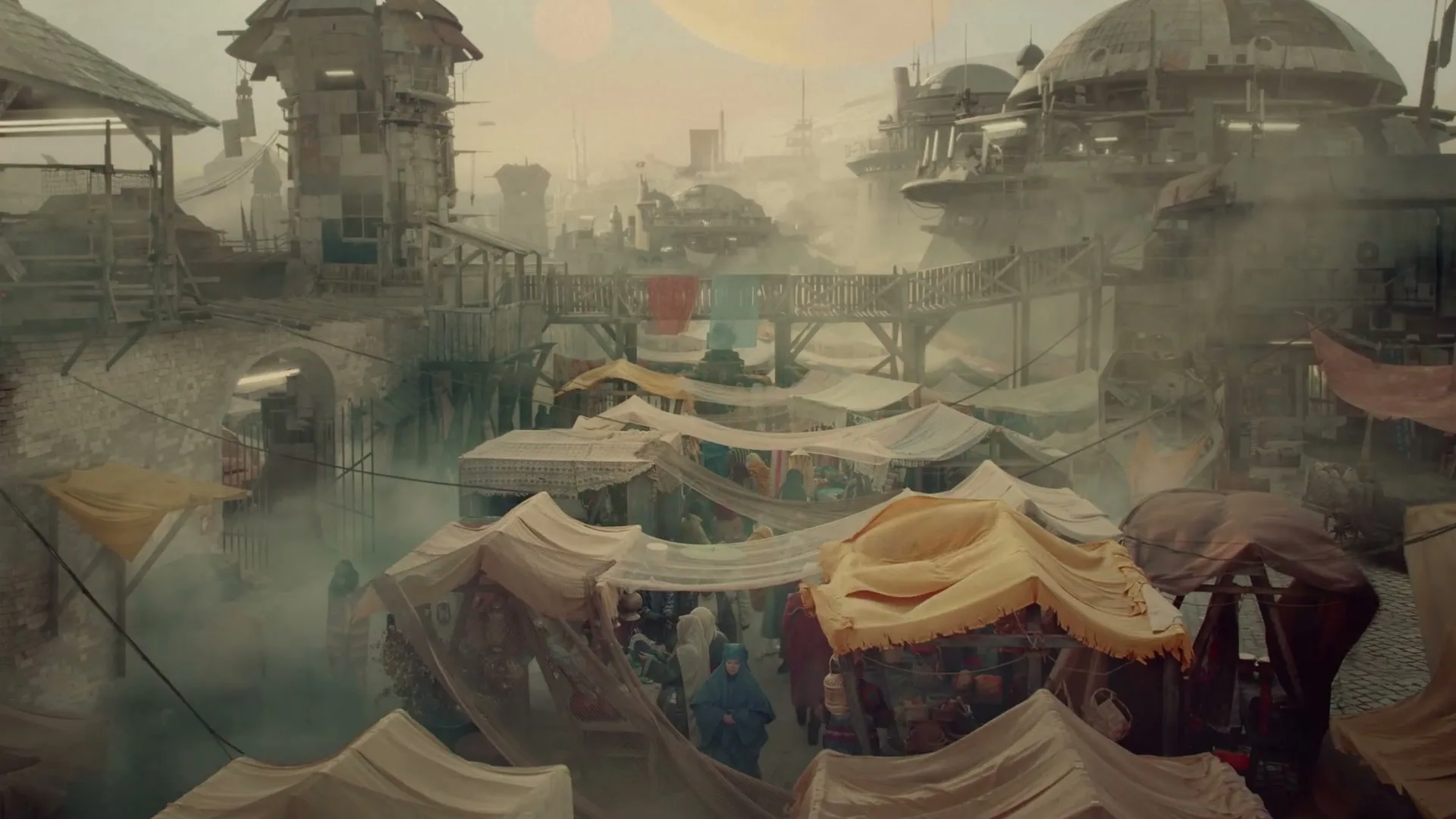 A wide shot of a bustling, futuristic marketplace with many people, tents, and buildings under a hazy sky with two large planets.