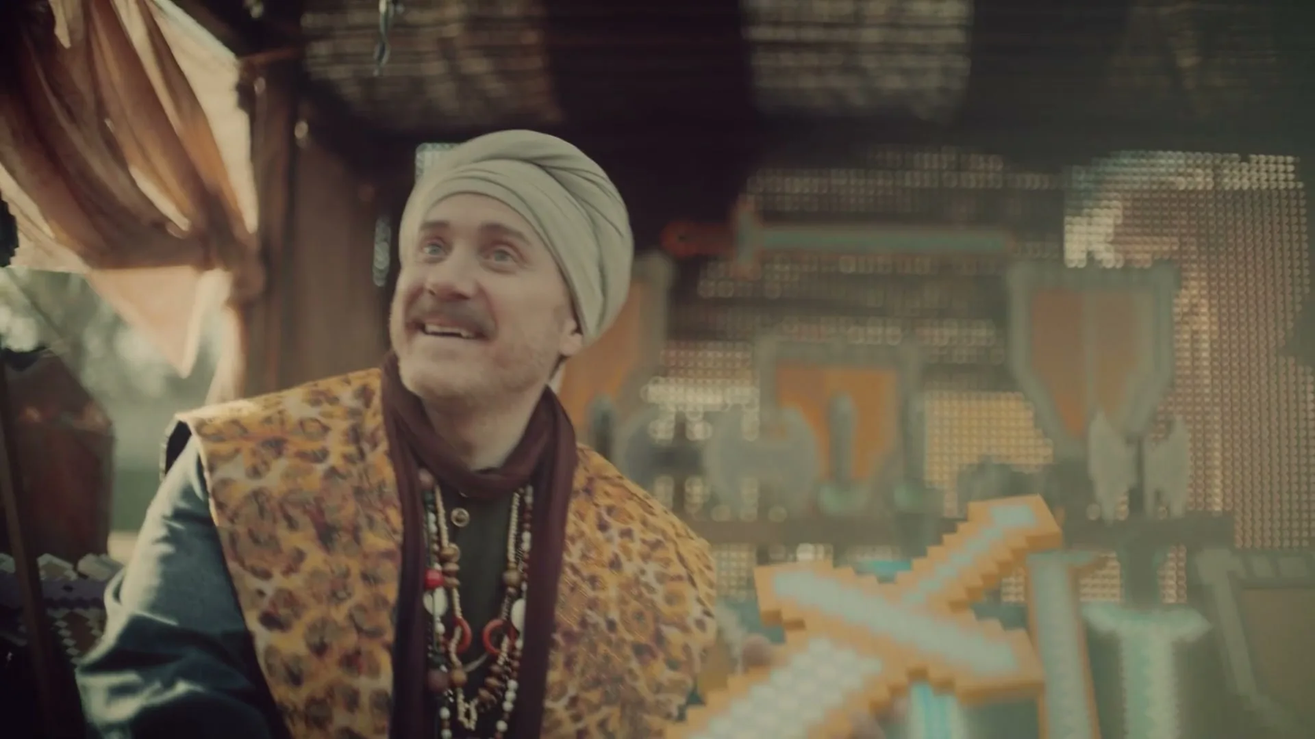A man in a turban and leopard print vest holds a pixelated sword, looking up with a smile in a market stall.