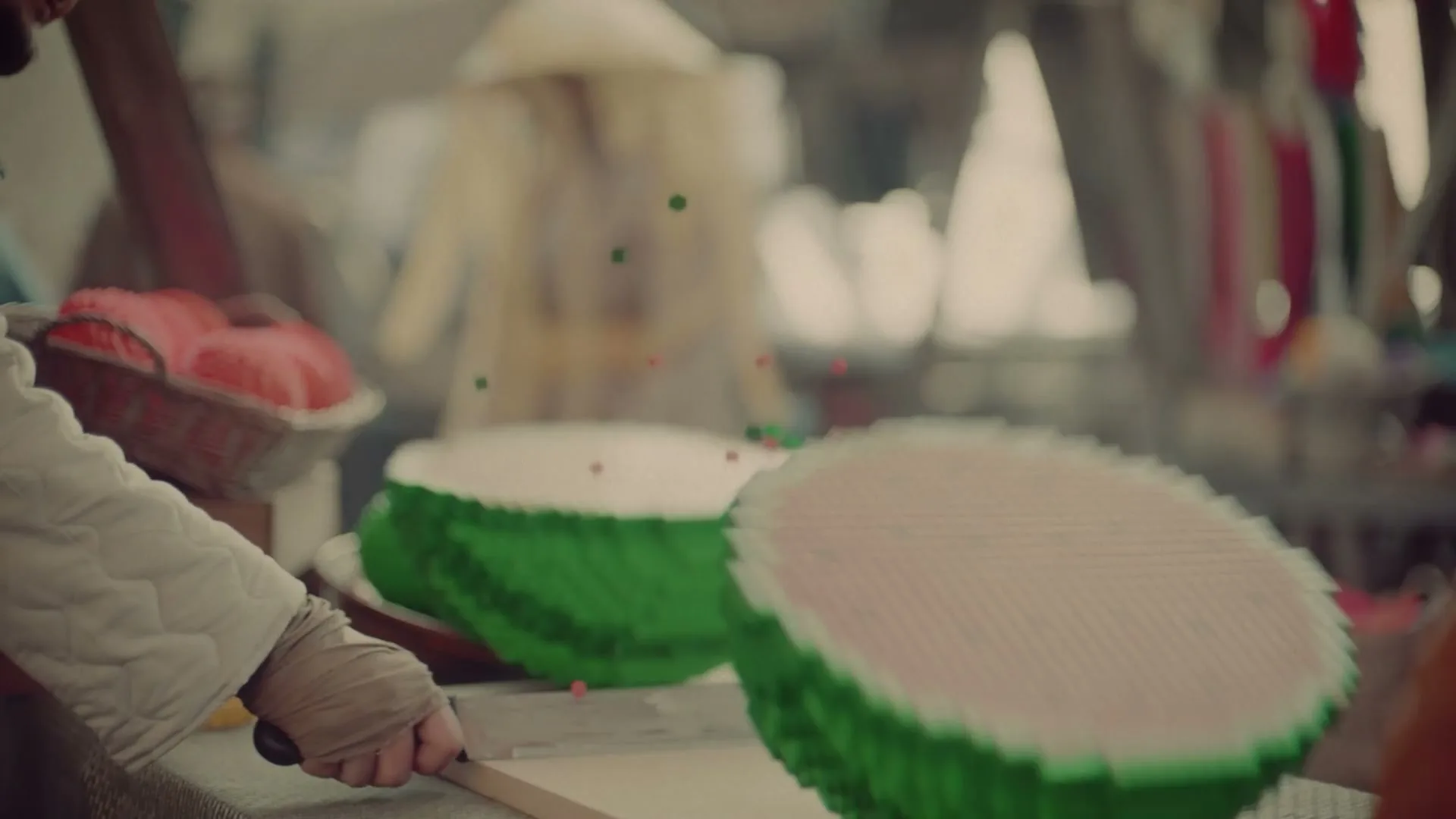 A person in a marketplace cuts a pixelated watermelon in half, revealing its red interior and scattering small pixel pieces.