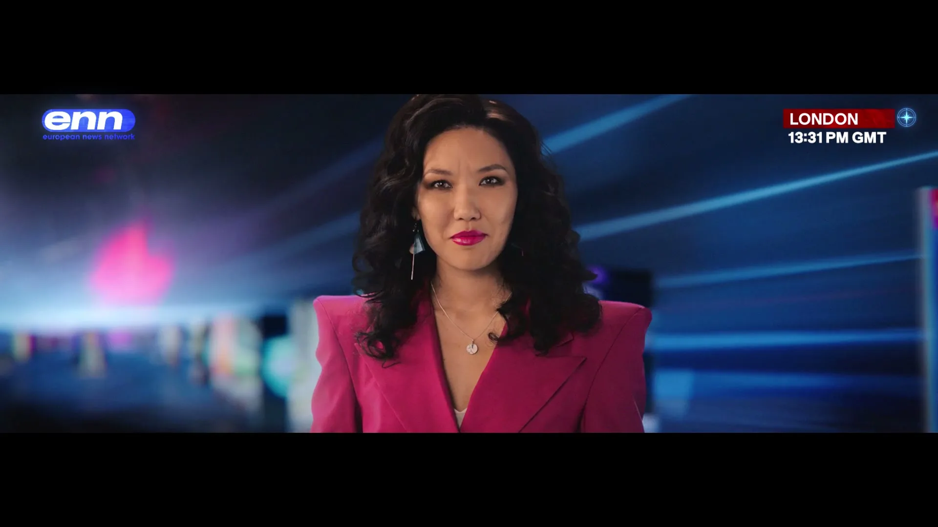 A female news anchor with dark curly hair and a pink blazer speaks directly to the camera in a virtual news studio.