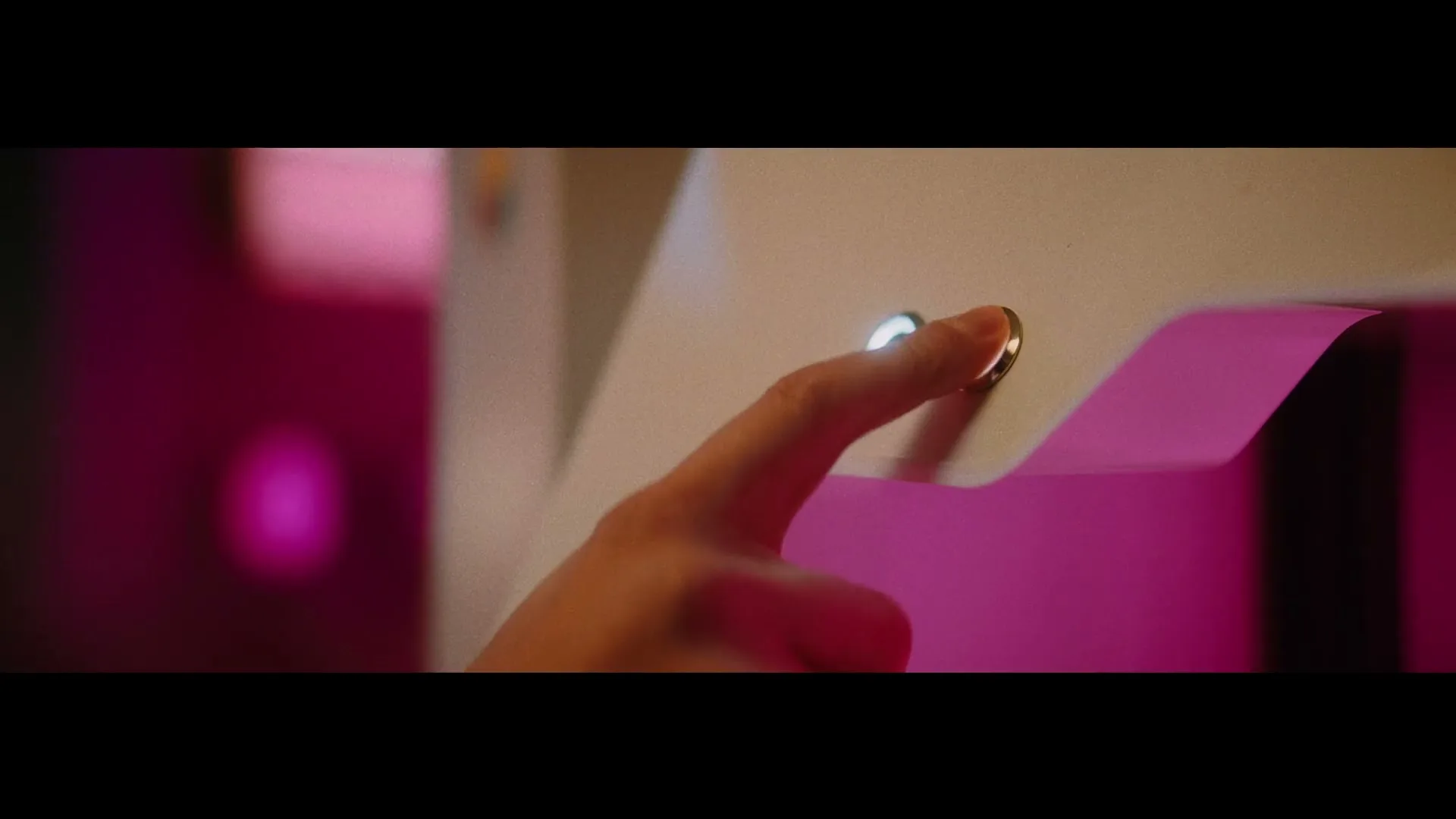 A person's finger presses a glowing button on a futuristic device, with a vibrant magenta background.
